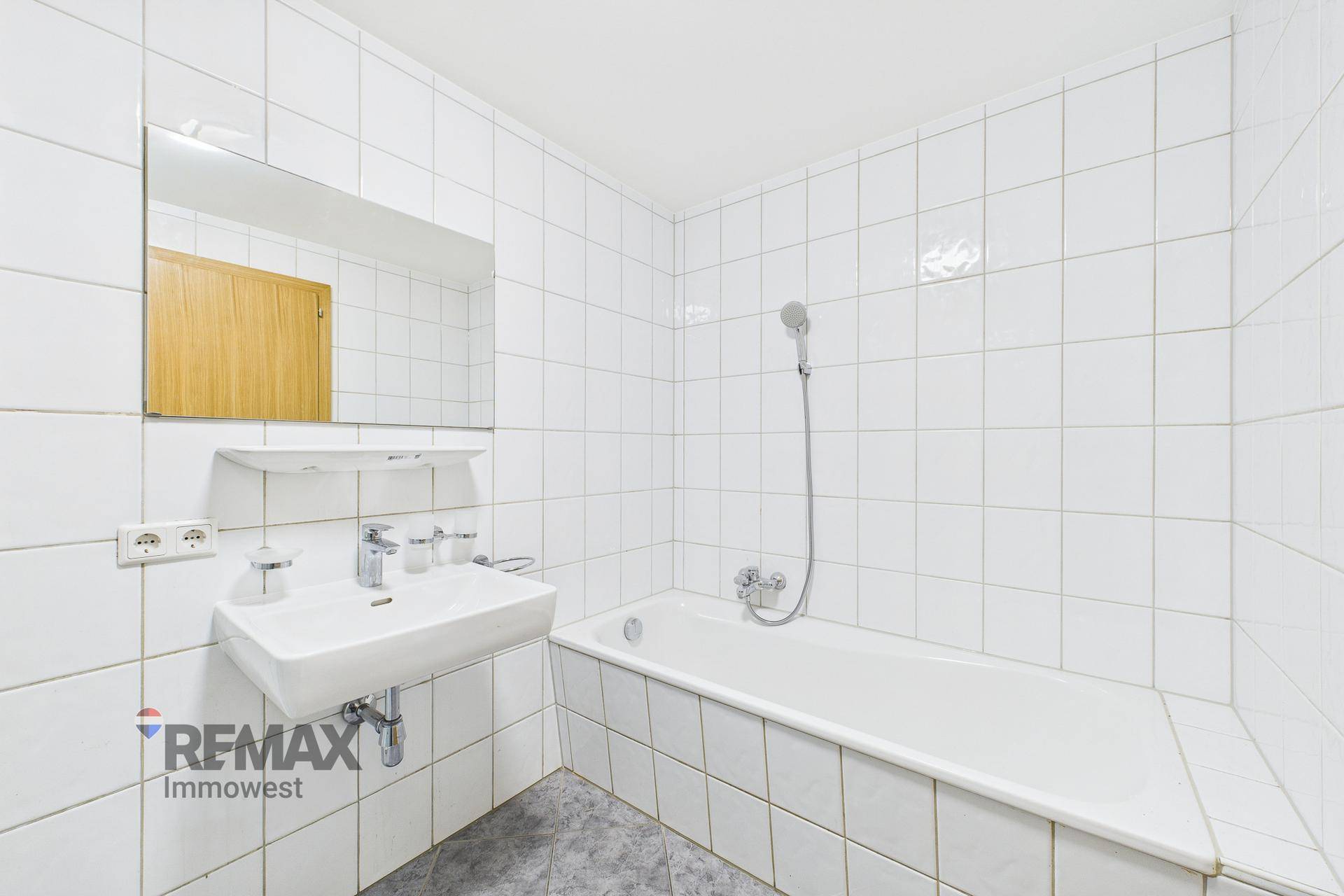 Gefliestes Badezimmer mit Badewanne, Waschbecken und Spiegel, in schlichtem Design gehalten.