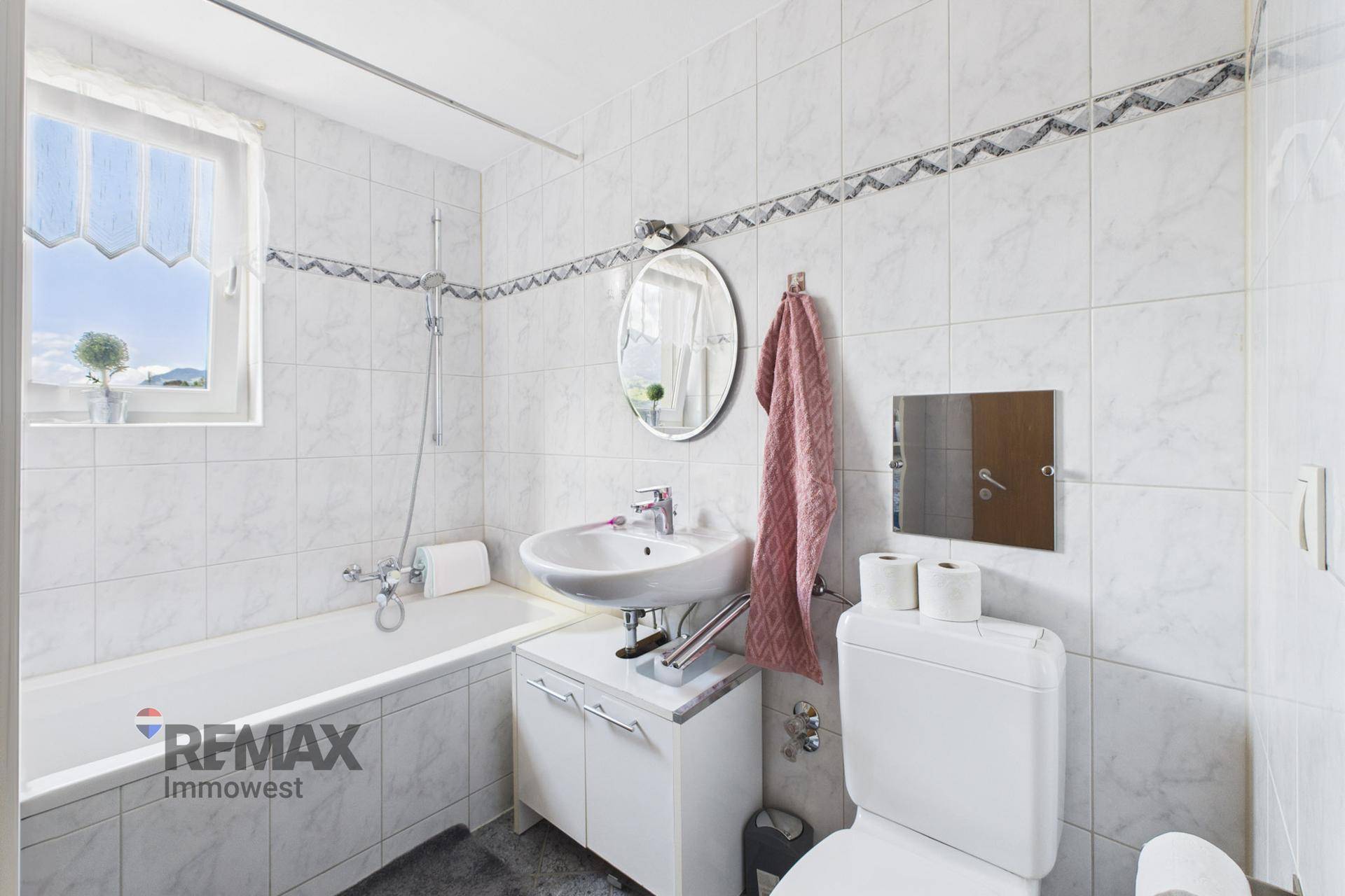 Gefliestes Badezimmer mit Badewanne, WC, Waschbecken und Fenster für Tageslicht.