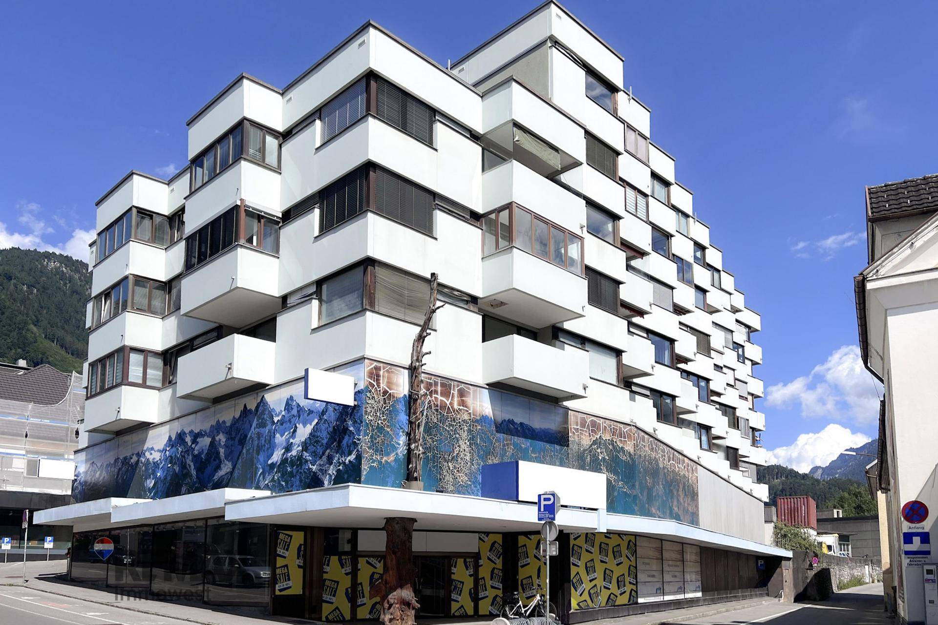 Modernes Gebäude mit gestufter Fassade und künstlerischer Bergmalerei im unteren Bereich.
