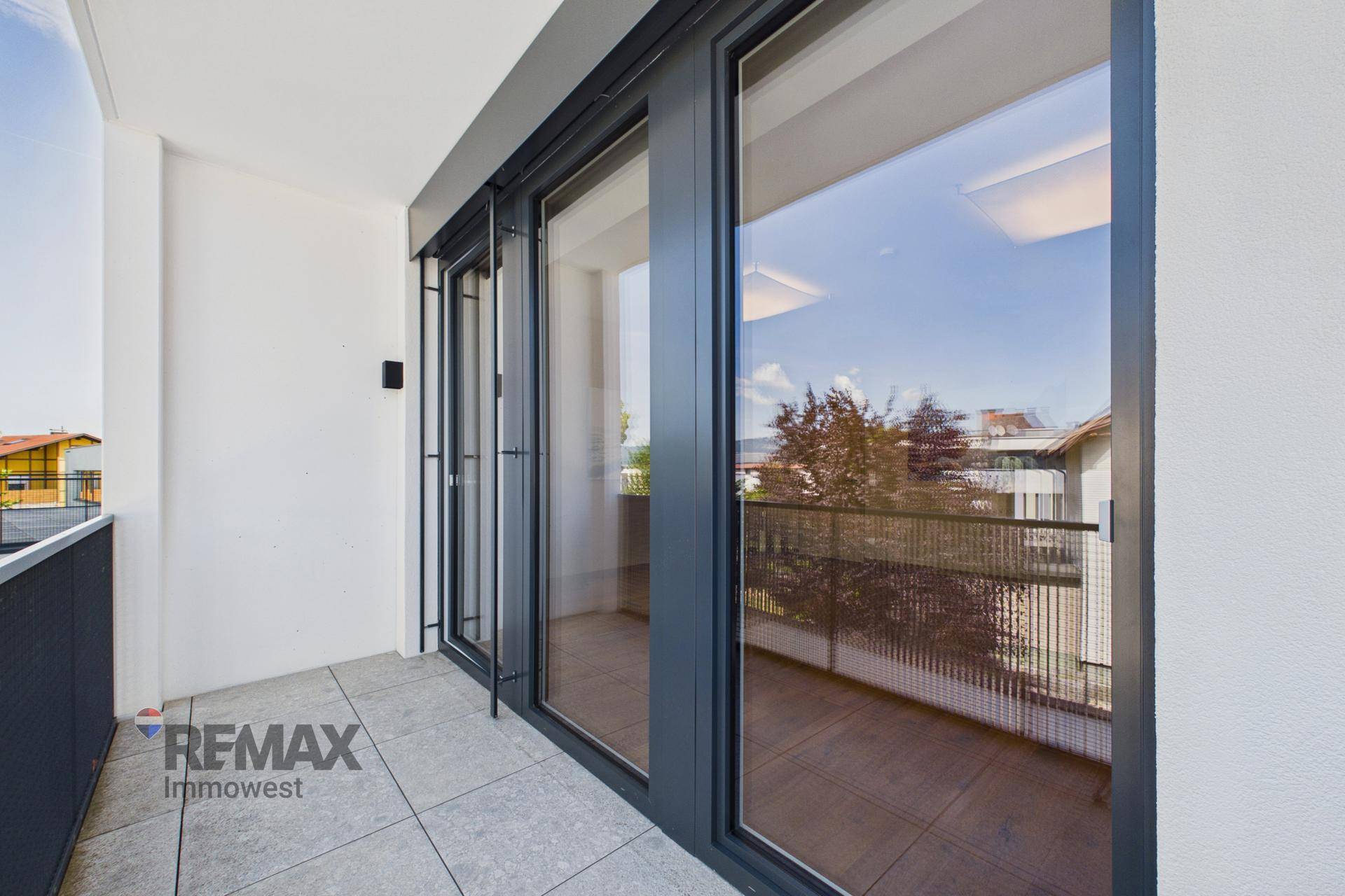 Moderner Balkon mit großen Glasschiebetüren, Fliesenboden und robustem Metallgeländer.