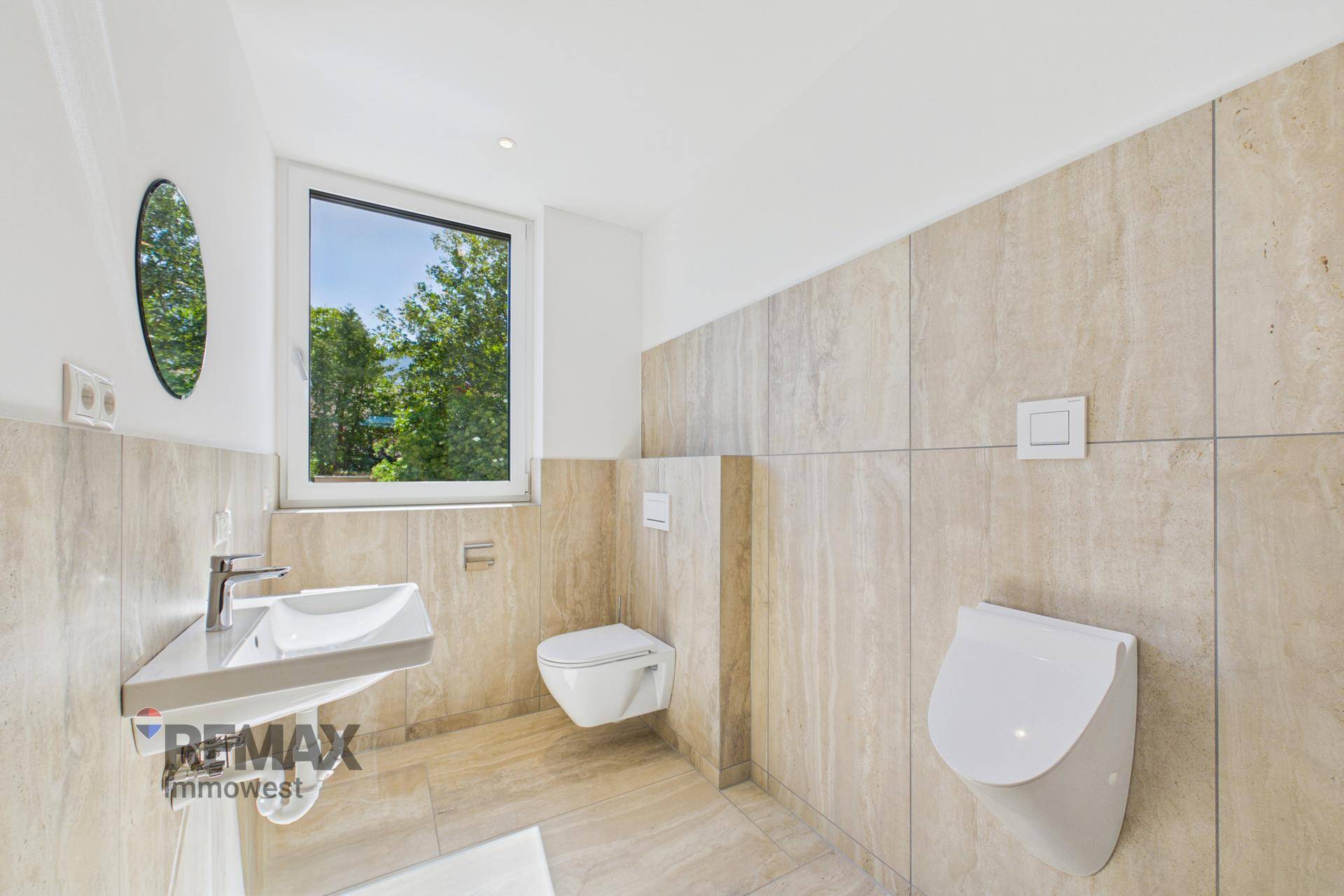 Helles Badezimmer mit beigen Fliesen, wandhängendem WC, Urinal und einem Fenster.