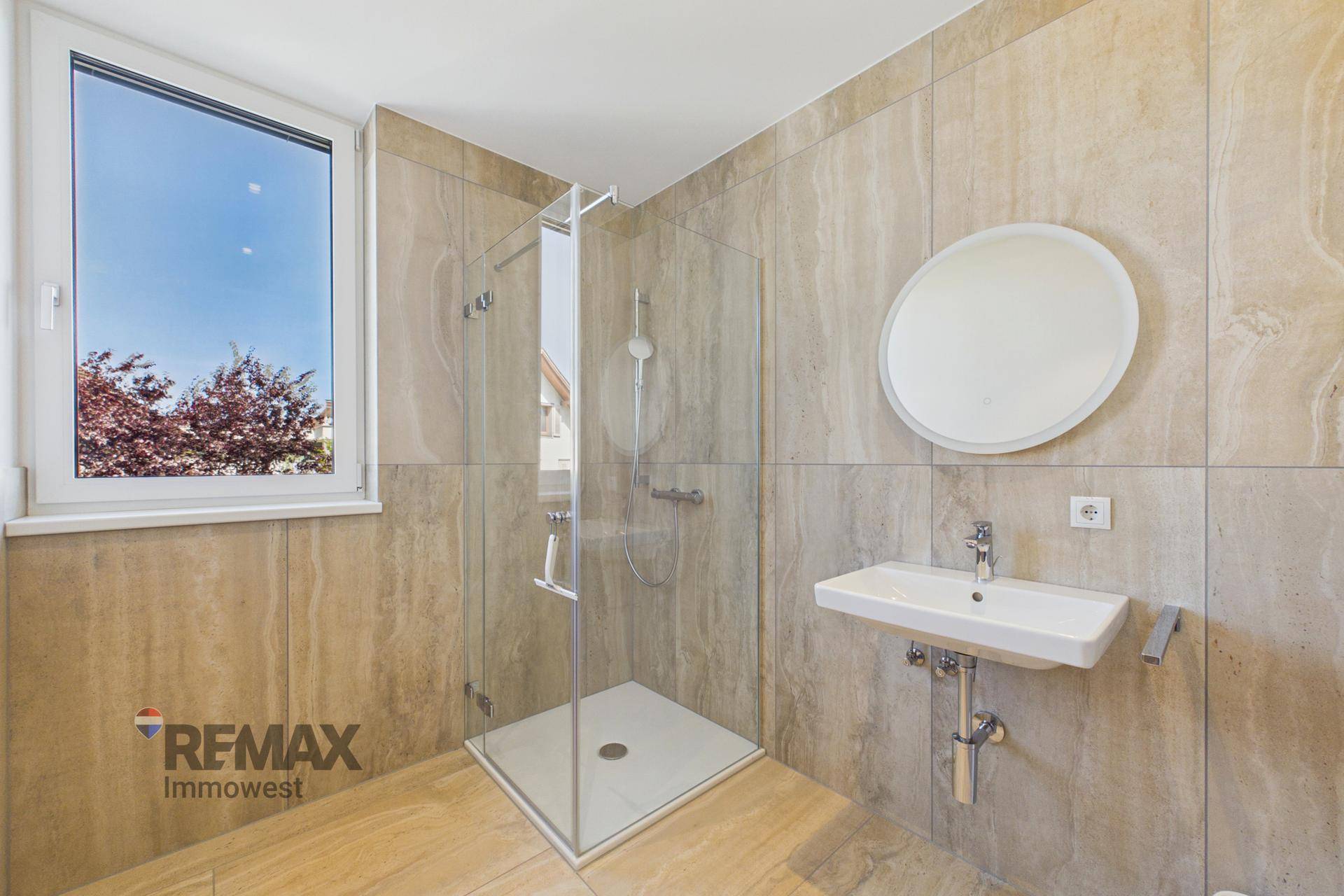 Modernes Badezimmer mit beigen Fliesen, begehbarer Dusche, Waschbecken und einem Fenster.