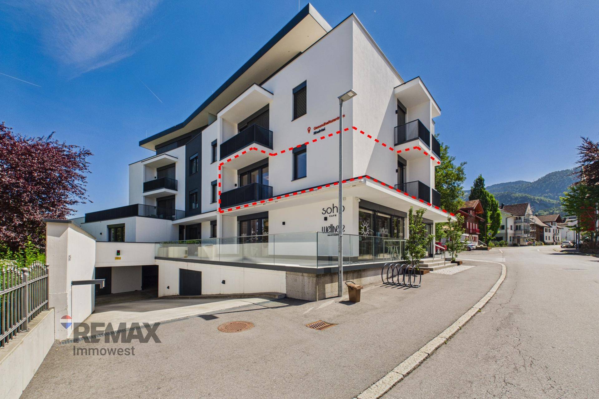 Modernes Gebäude mit weißer Fassade und schwarzen Balkonen, umrandet von einer roten Linie.
