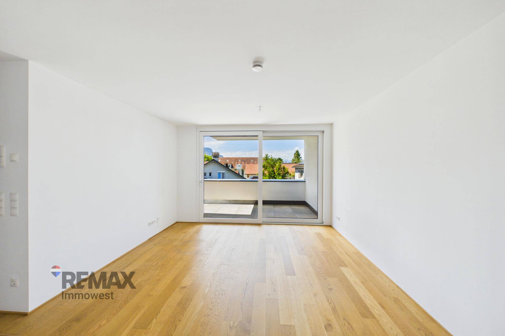 Geräumiger, leerer Wohnbereich mit hellem Parkettboden und großen Schiebetüren zum Balkon.