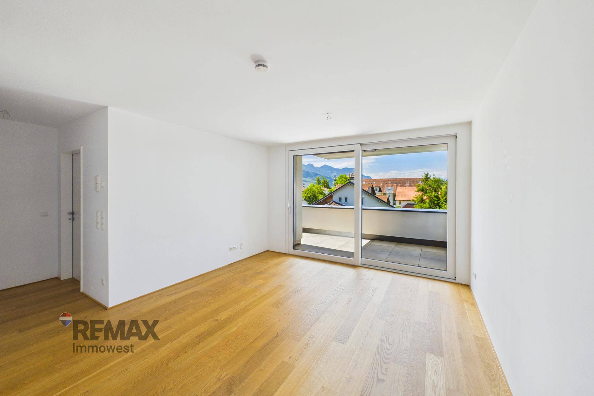 Heller Wohnraum mit Parkettboden und großzügigem Zugang zu einem Balkon mit Bergblick.