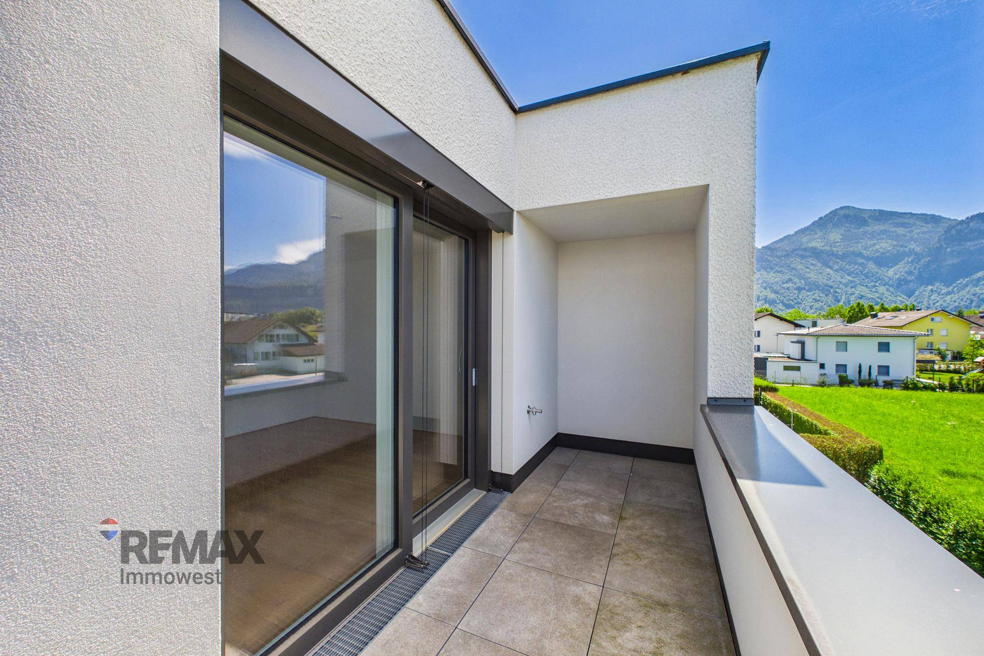 Kleinerer Balkon mit Fliesenboden und Blick auf die grüne Umgebung und Berge.
