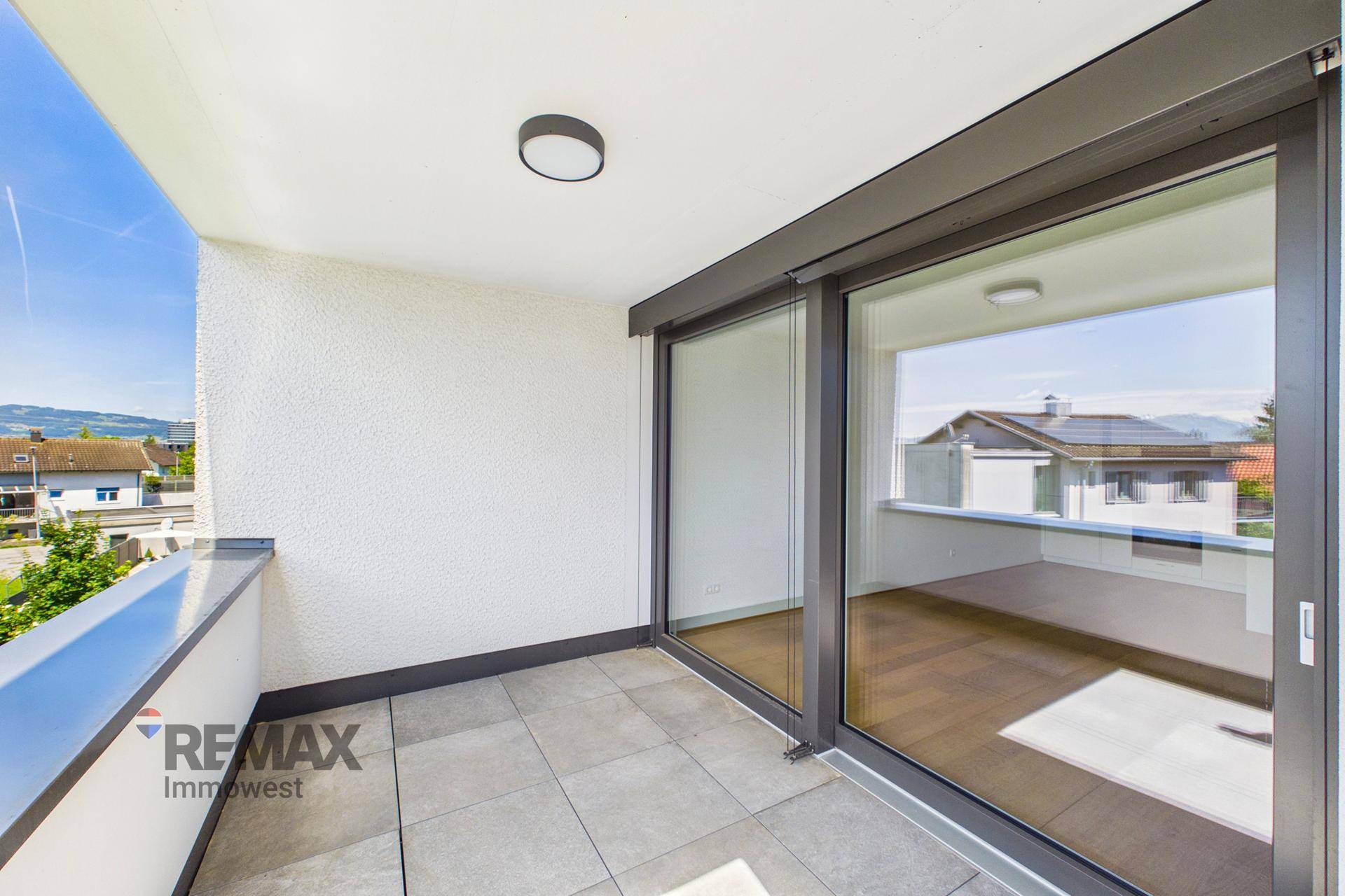 Heller Balkon mit Fliesenboden und großen Schiebetüren, die viel Licht in den Innenraum lassen.