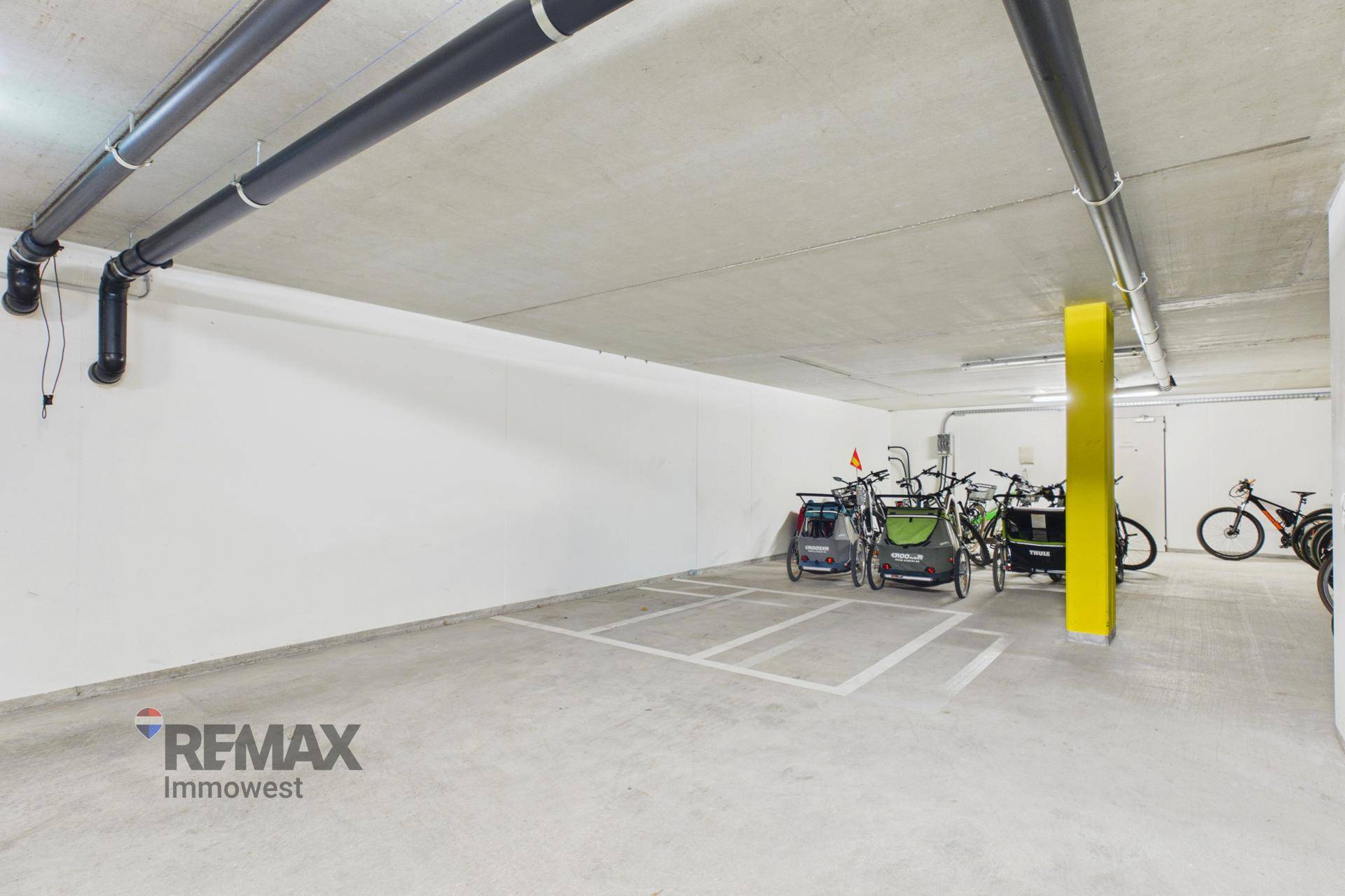 Geräumige Tiefgarage mit Abstellmöglichkeiten für Fahrräder und sichtbaren Versorgungsleitungen.