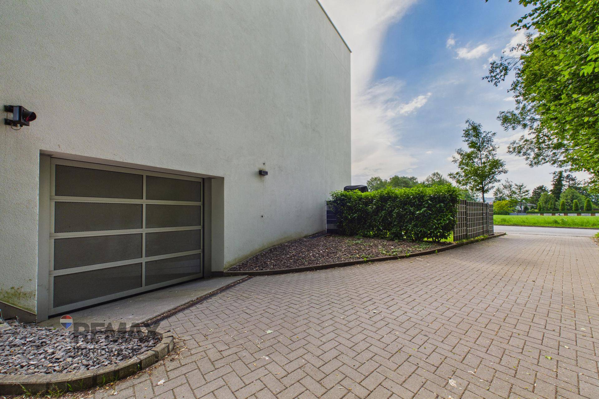 Garageneinfahrt mit modernem Tor und gepflastertem Vorplatz neben einer Hecke.