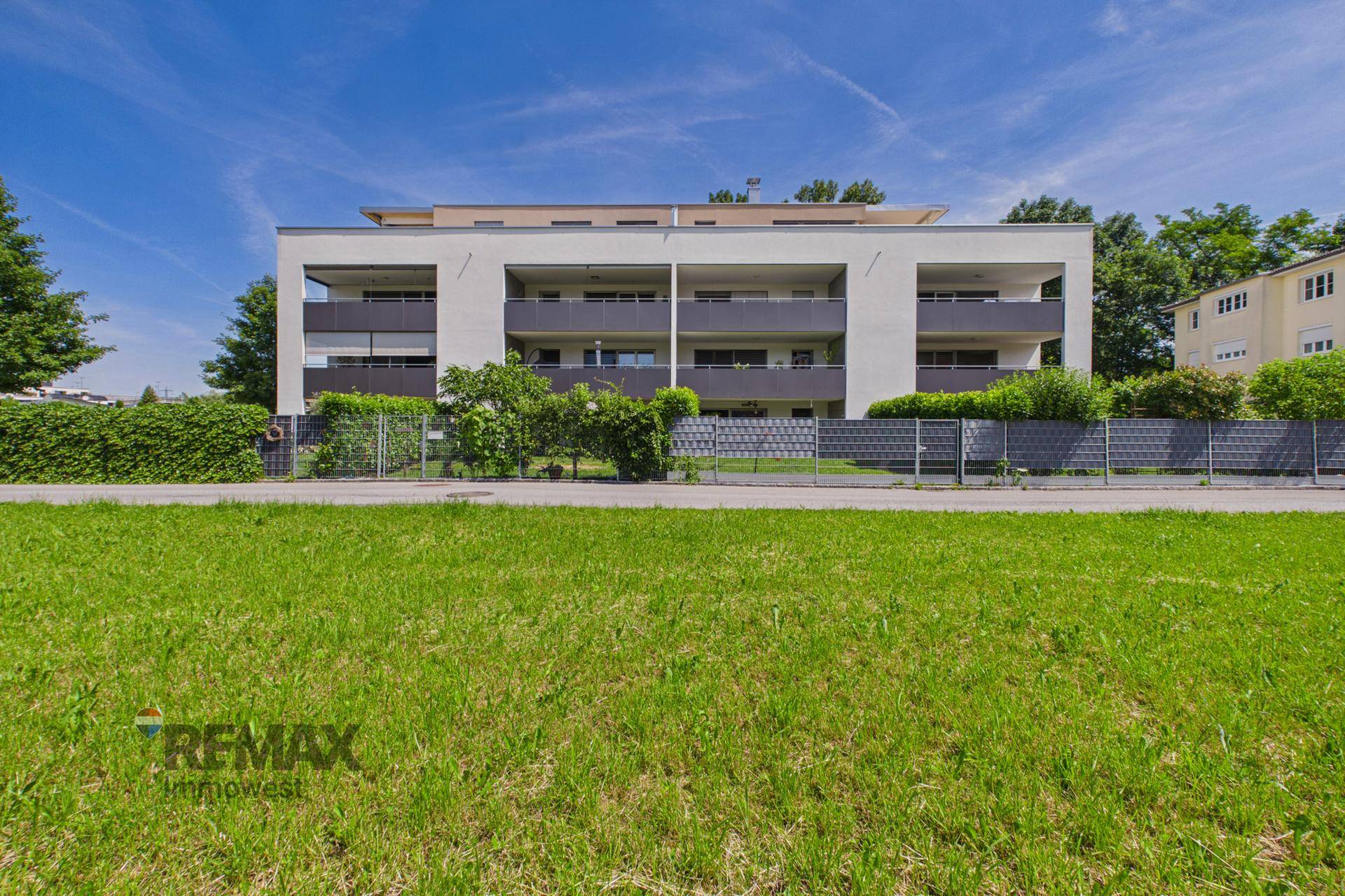 Ansicht der modernen Fassade eines Mehrfamilienhauses mit Balkonen und gepflegter Hecke.