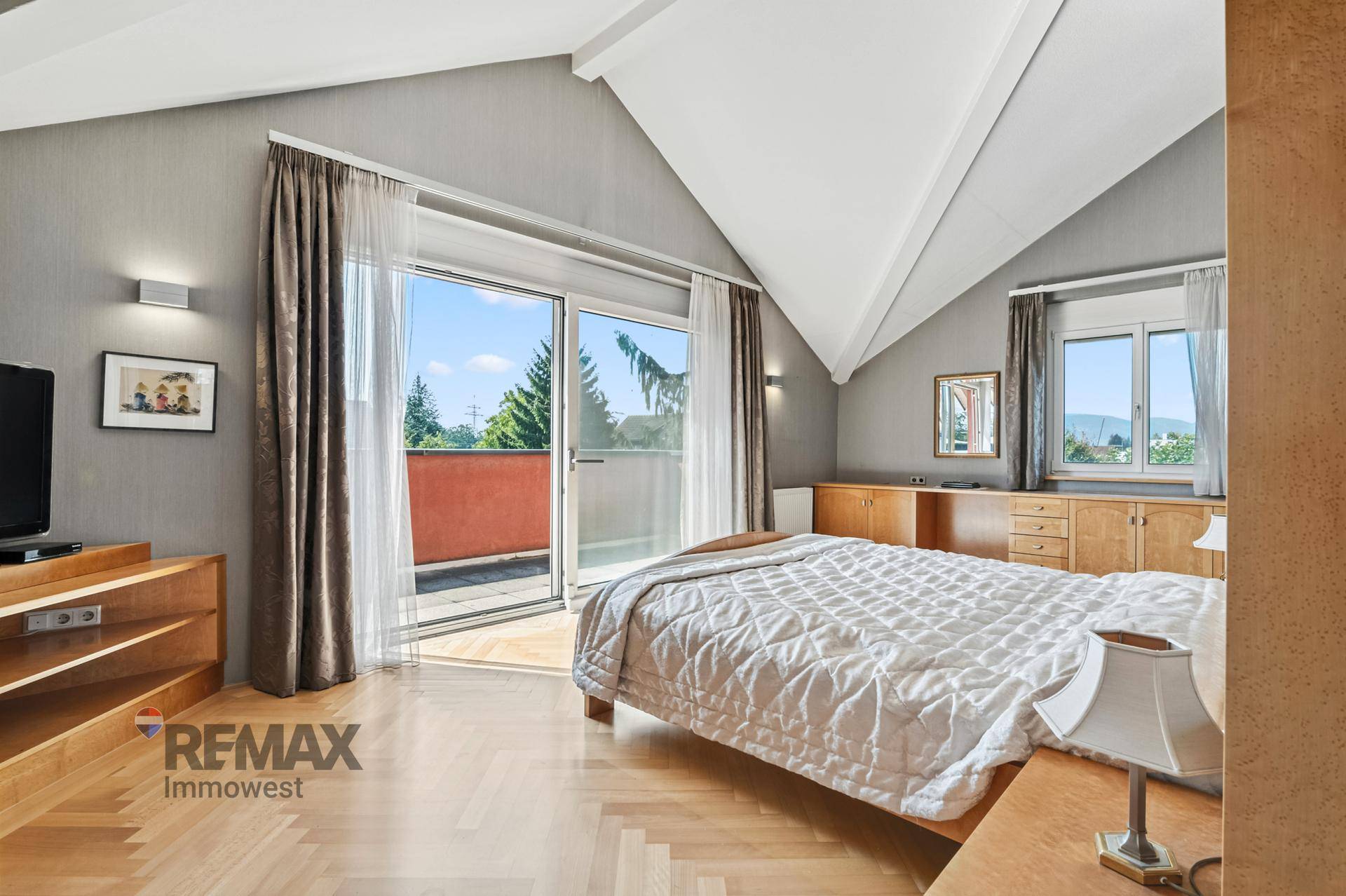 Helles Schlafzimmer mit Holzboden, Dachschräge und direktem Zugang zu einem Balkon.
