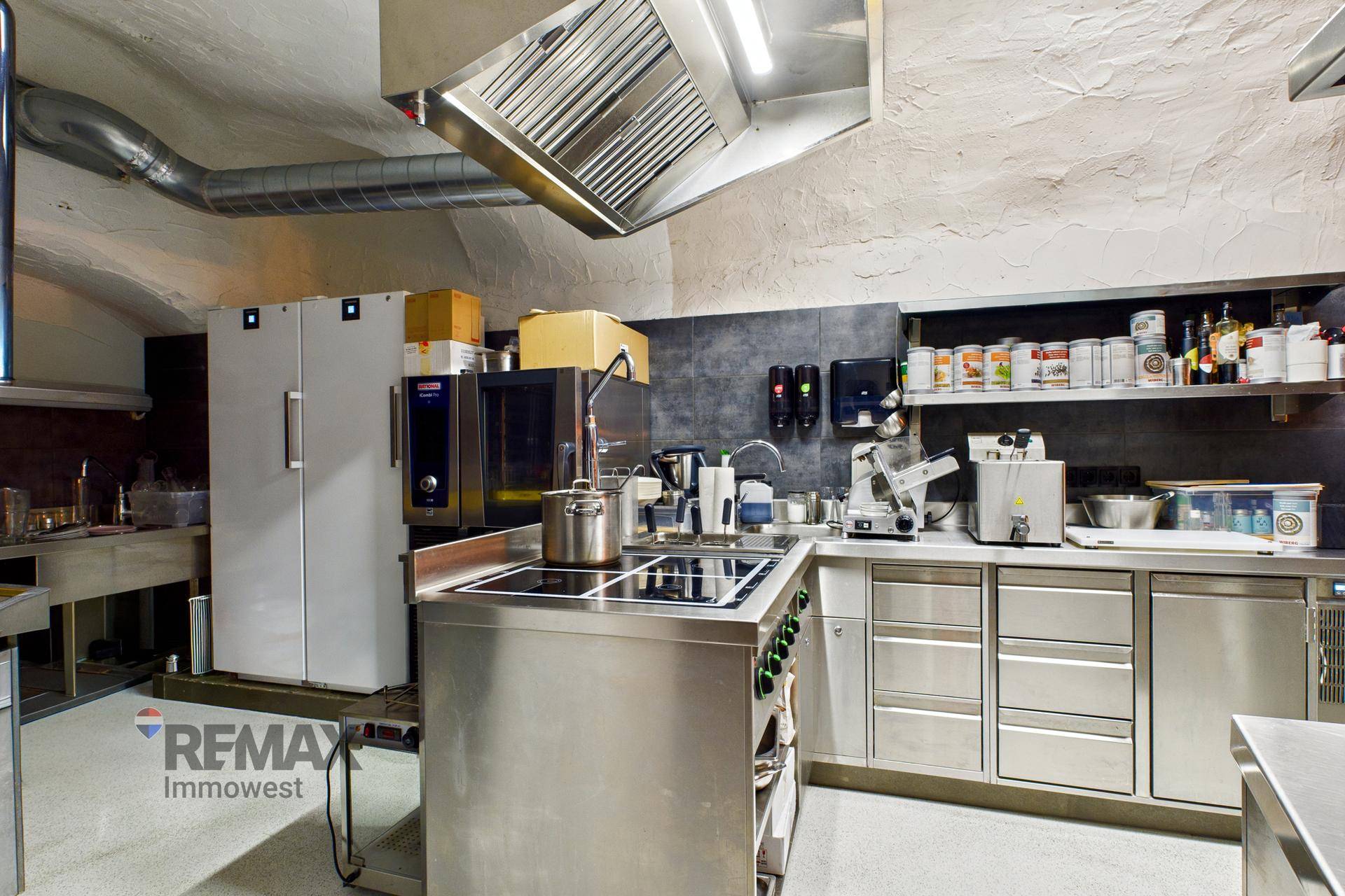 Professionelle Gastroküche mit Edelstahloberflächen, Dunstabzugshaube und modernen Geräten.