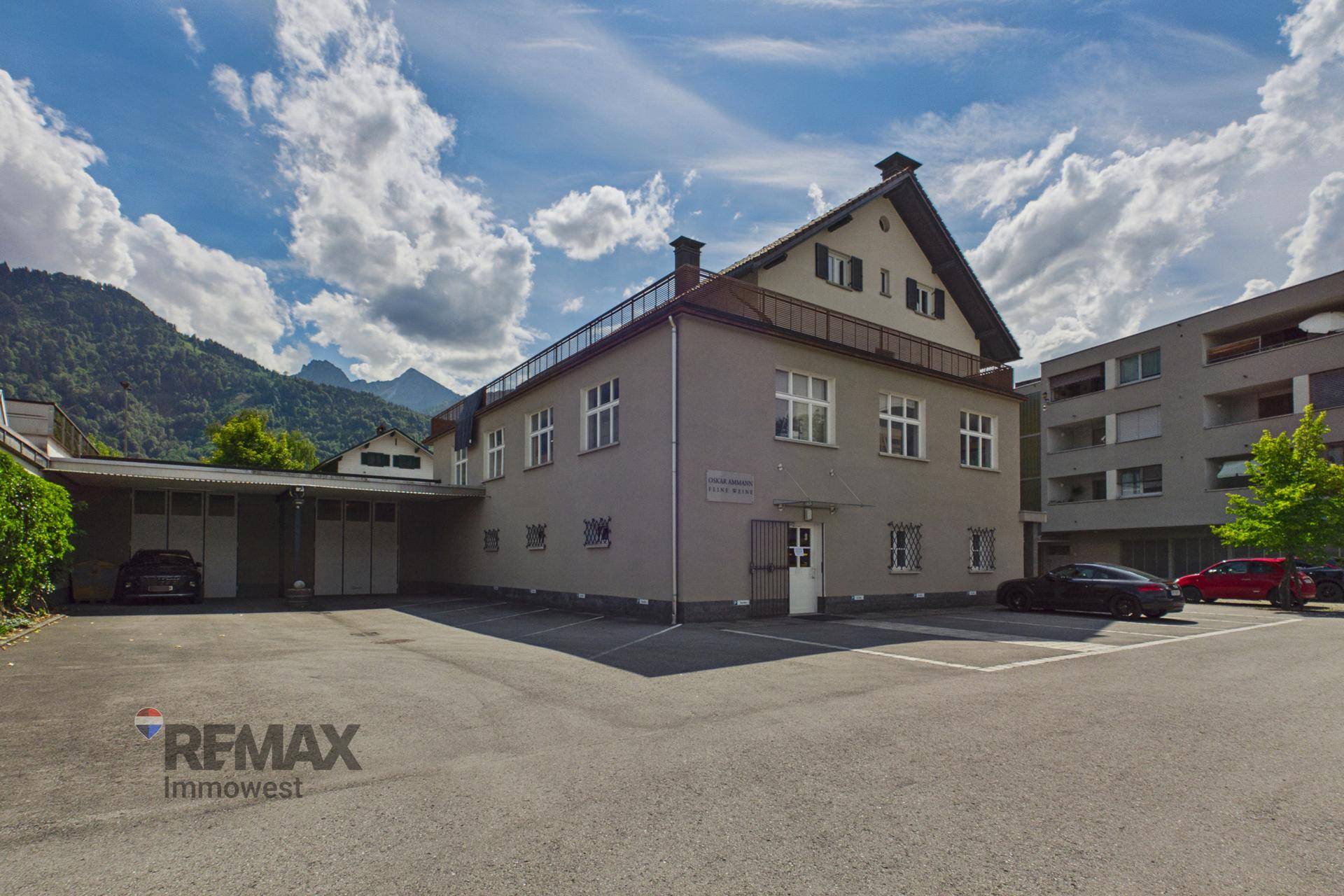 Ansicht des Gebäudes mit Parkplätzen davor und Bergen im Hintergrund unter blauem Himmel.