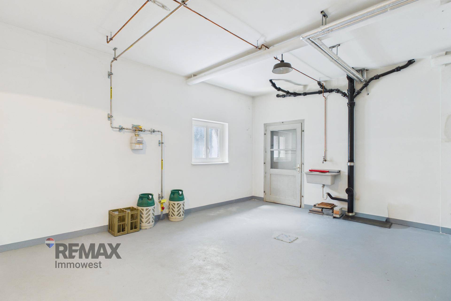 Heller Mehrzweckraum mit Gasleitungen, Waschbecken und einem Fenster, ideal als Werkstatt oder Lager.