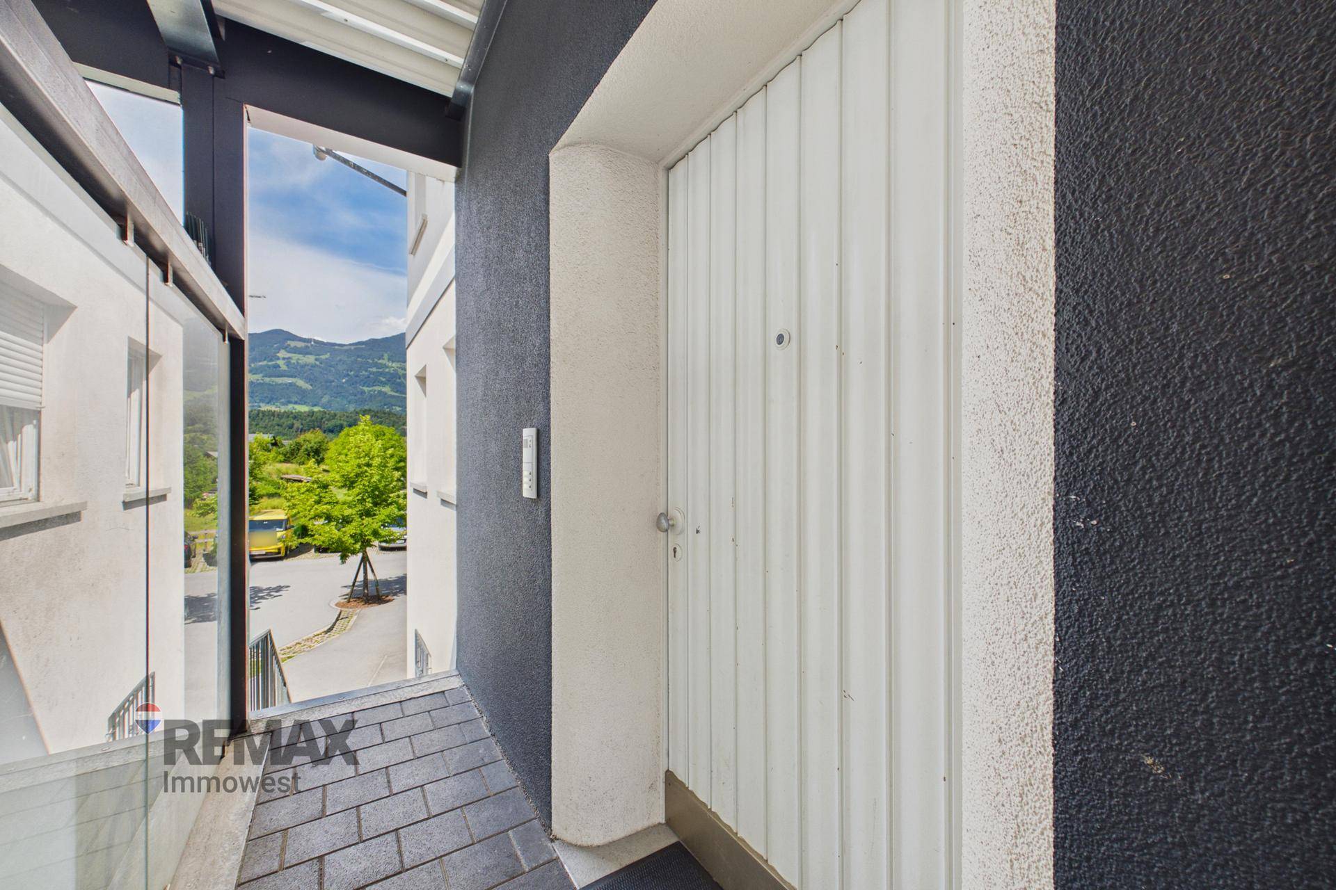 Moderner Eingangsbereich mit weißer Tür und dunkler Fassade, umgeben von Glas und Metall.
