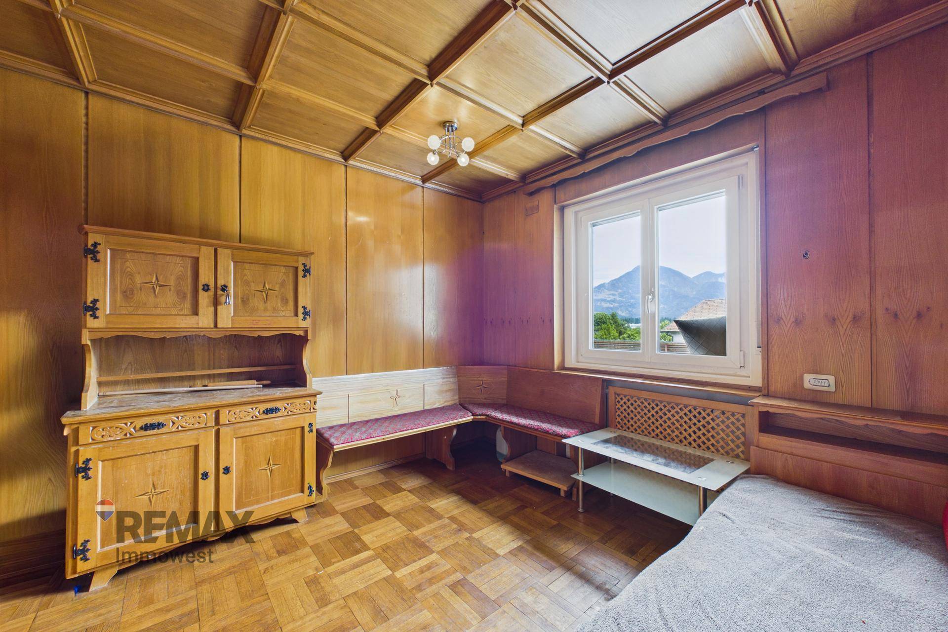 Gemütliches Zimmer mit Holztäfelung, Kassettendecke und Bergblick durch das Fenster.
