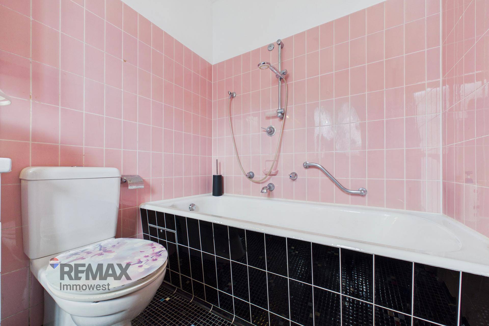 Badezimmer mit auffälligen rosa Fliesen, Toilette und einer Badewanne mit schwarzen Akzenten.