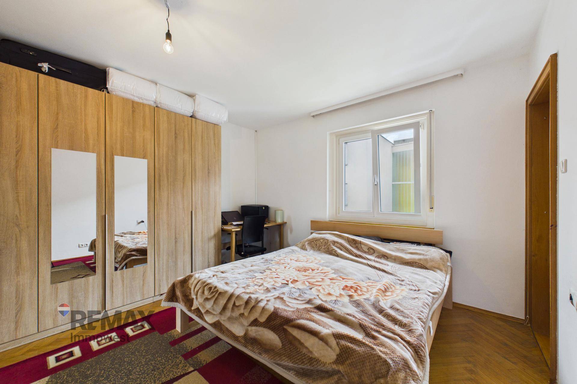 Schlafzimmer mit großem Holzschrank, Doppelbett und einem Fenster für natürliches Licht.