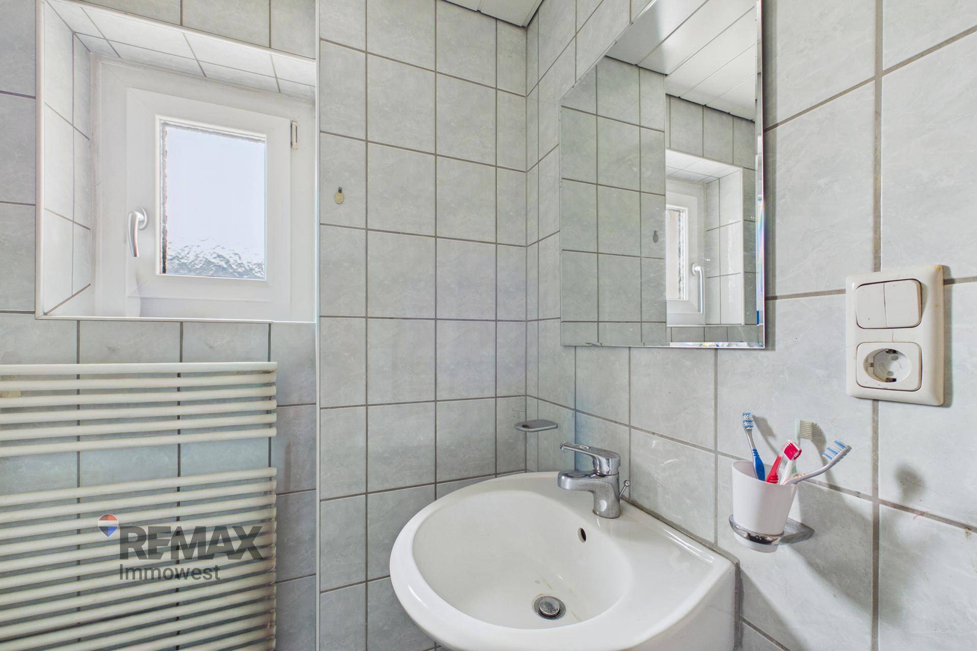 Kleines Badezimmer mit grauen Fliesen, Eckwaschbecken und beheiztem Handtuchhalter.