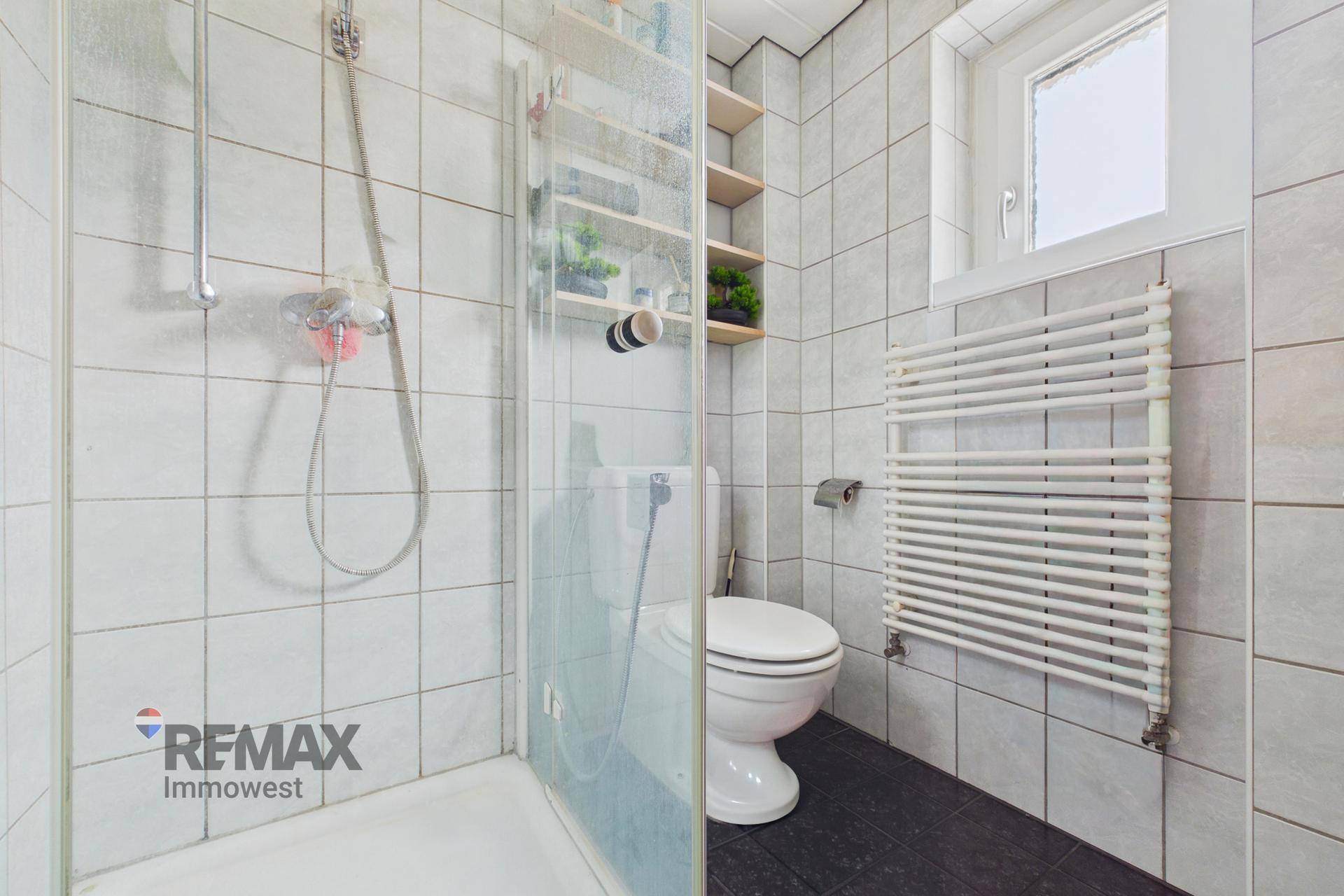 Badezimmer mit Duschkabine, Toilette, beheiztem Handtuchhalter und Fenster.