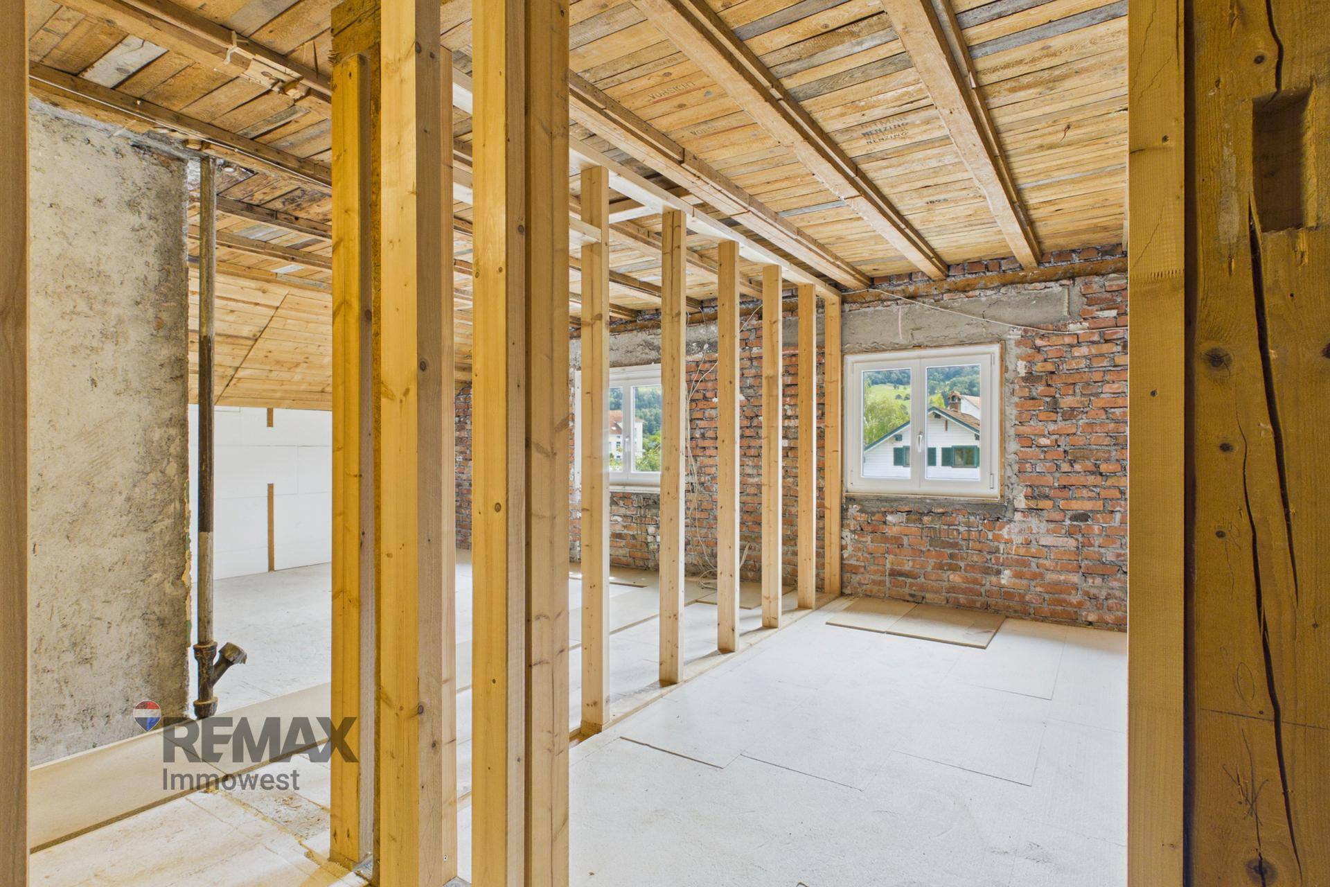 Innenraum im Rohbau mit freiliegenden Ziegelwänden und Holzbalken.