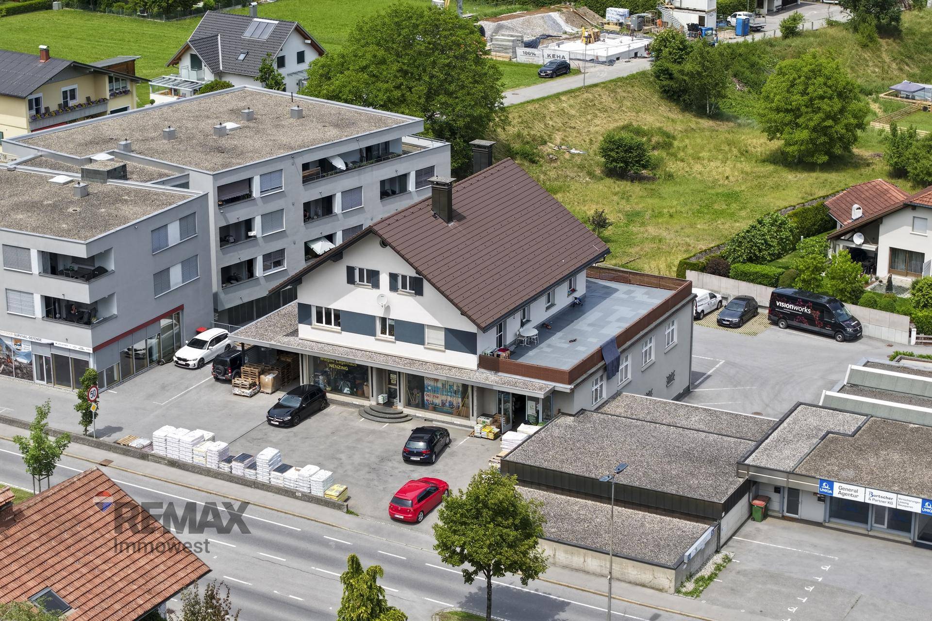 Luftaufnahme eines Gebäudekomplexes mit Parkplätzen und umliegender Bebauung.