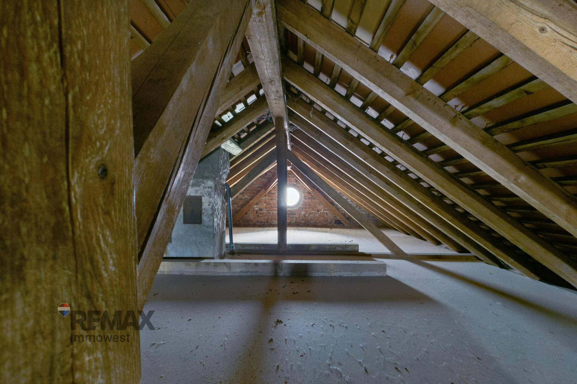 Dachboden mit sichtbarer Holzkonstruktion und einem kleinen runden Fenster.