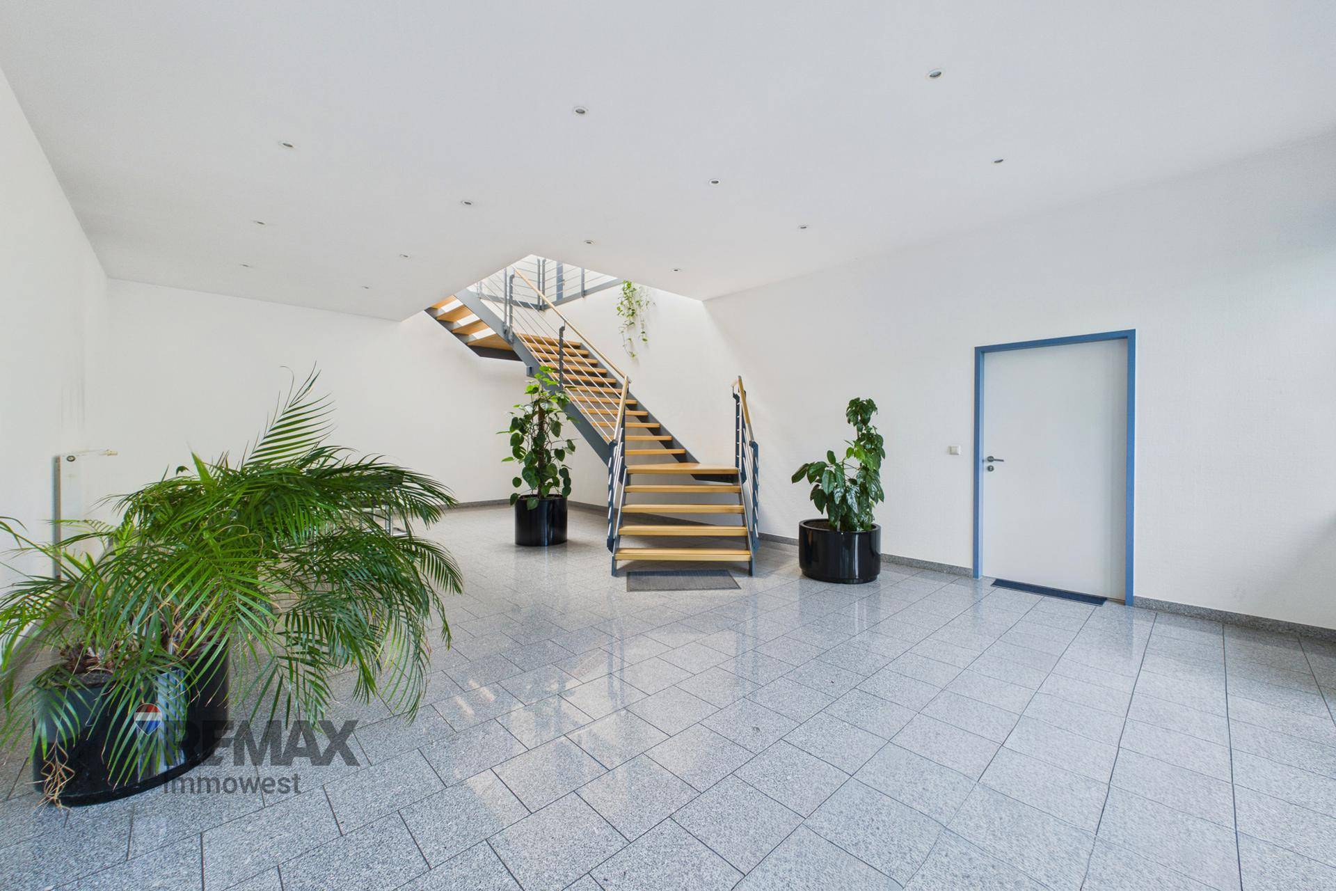 Heller Eingangsbereich mit Granitfliesen, einer modernen Holztreppe und dekorativen Pflanzen.