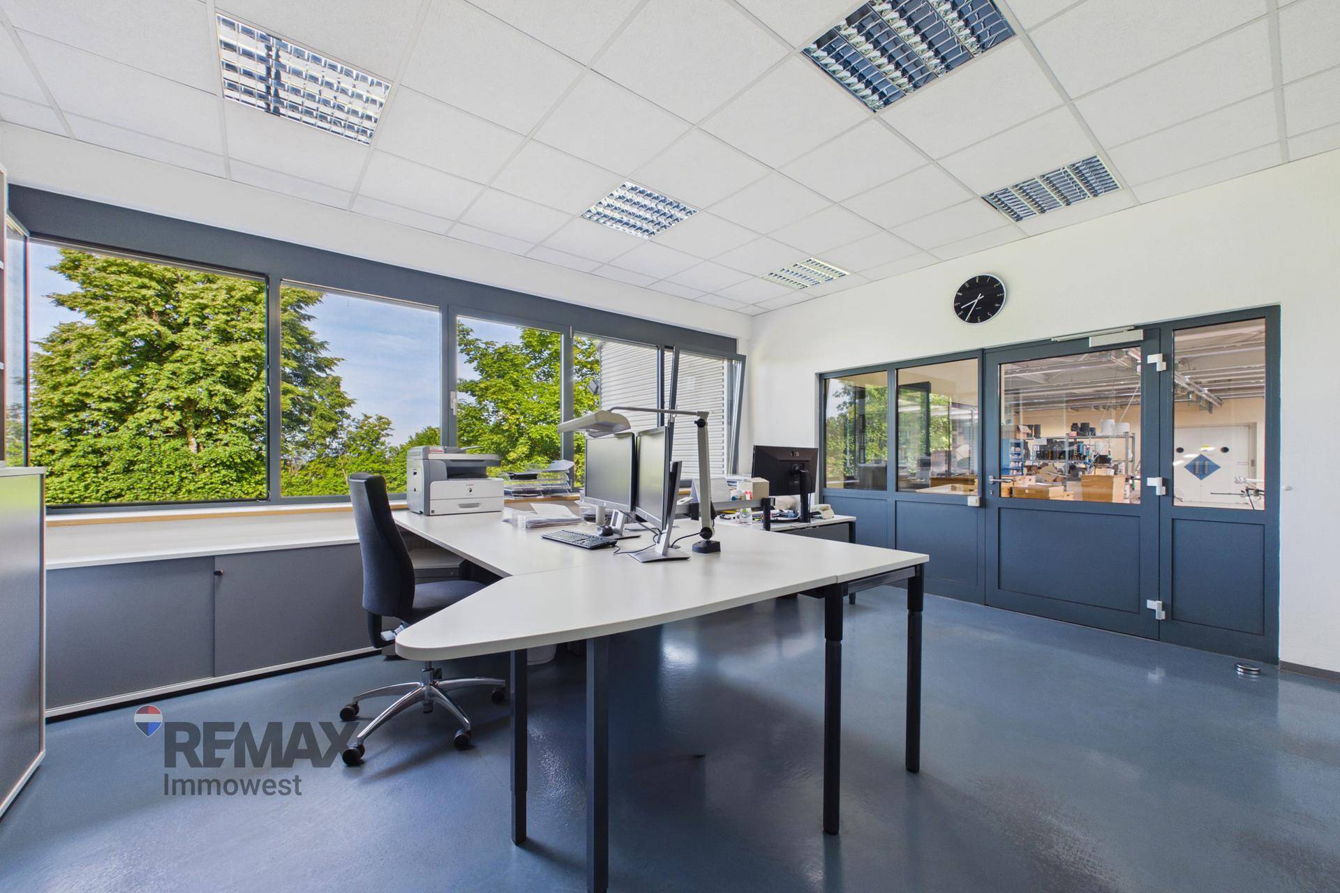 Helles Büro mit modernen Möbeln, großen Fenstern und einer Glastrennwand zu einem weiteren Bereich.