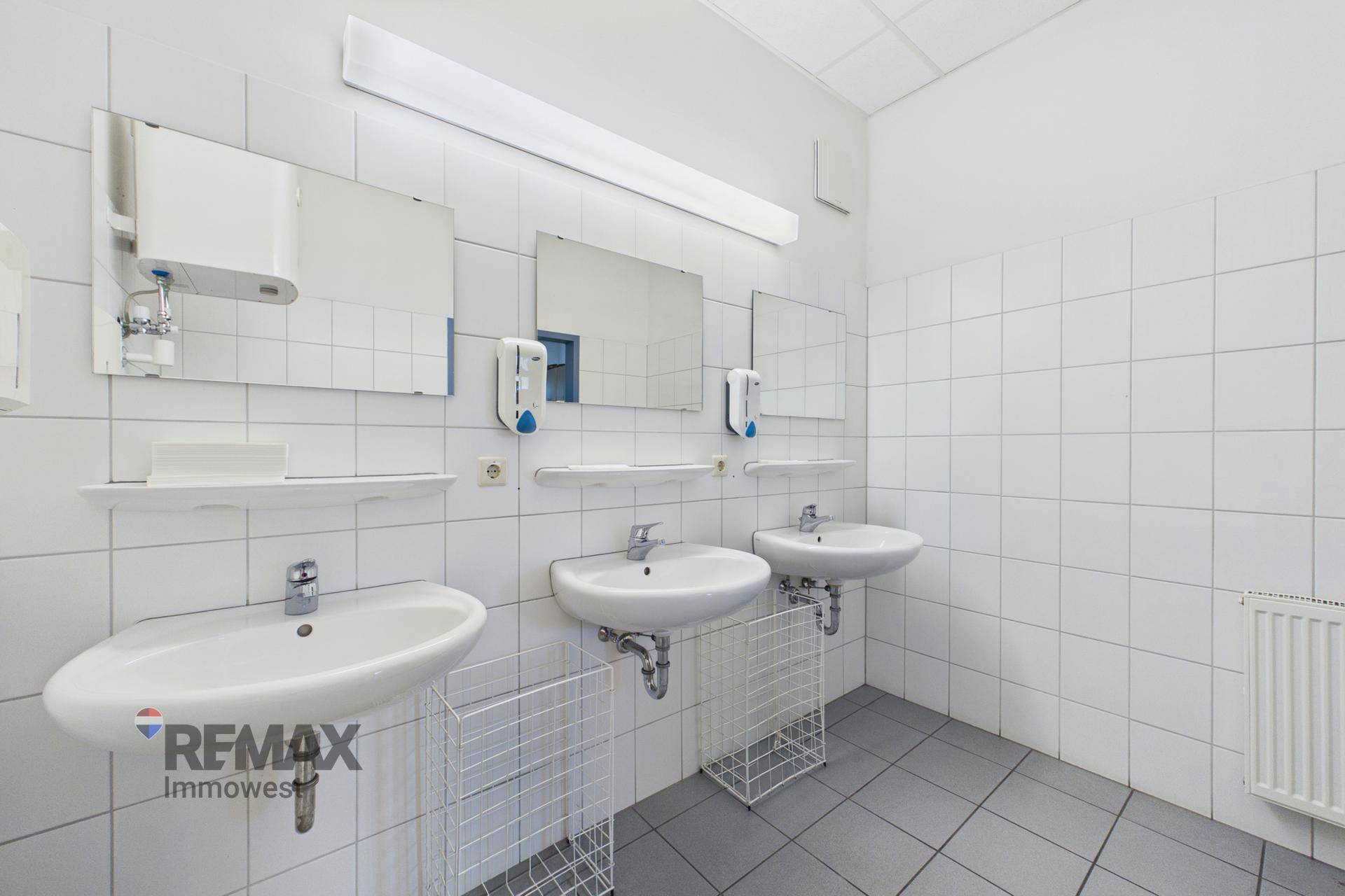 Waschraum mit mehreren Waschbecken, großen Spiegeln und weiß gefliesten Wänden.
