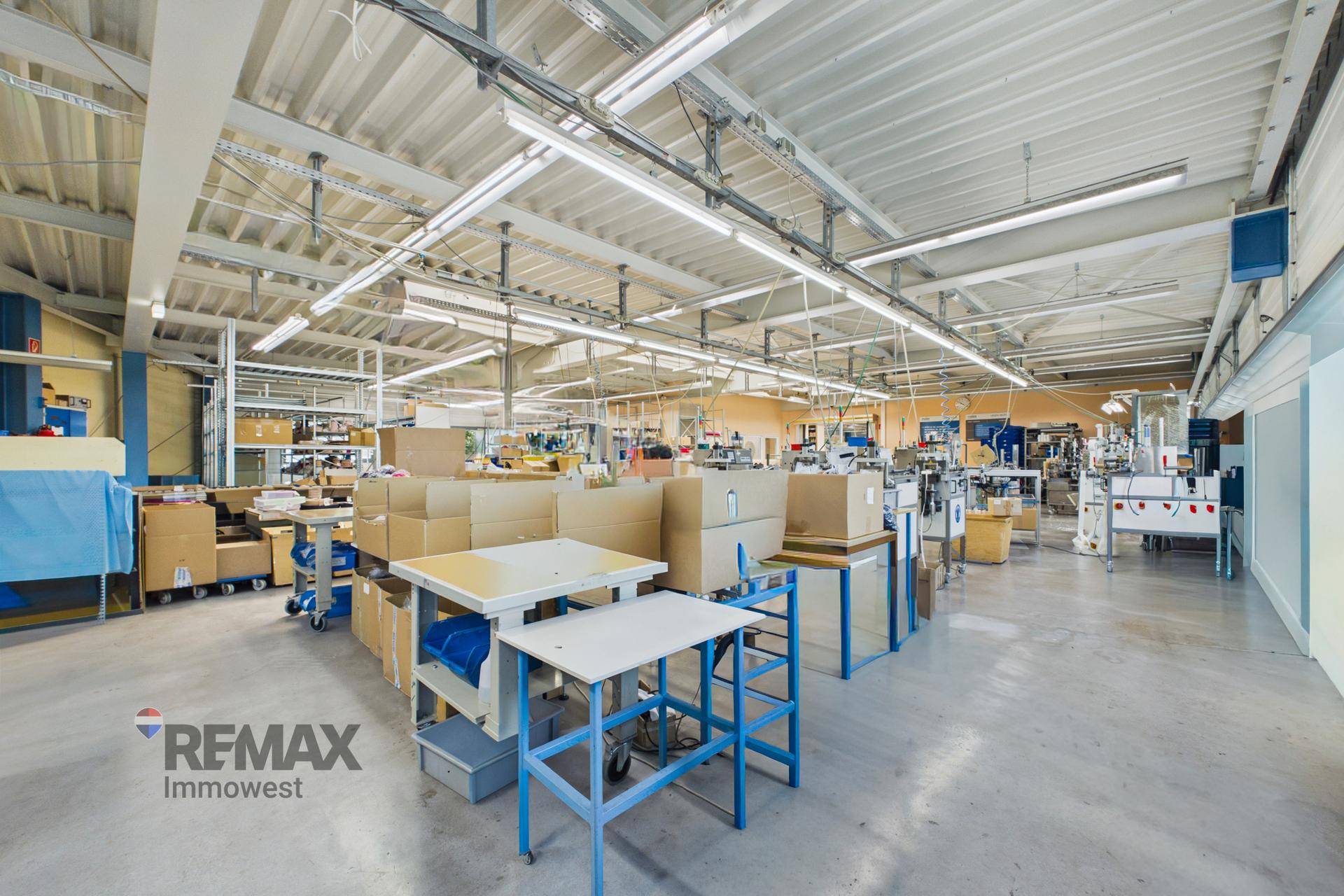 Große Produktionshalle mit vielen Arbeitsplätzen, Maschinen und einer hohen Decke.