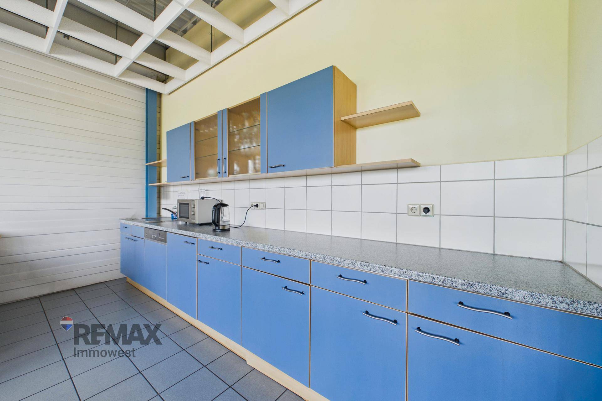 Einfache Küche mit blauen Schränken, weißem Fliesenspiegel und Arbeitsplatte, ausgestattet mit Mikrowelle und Spüle.
