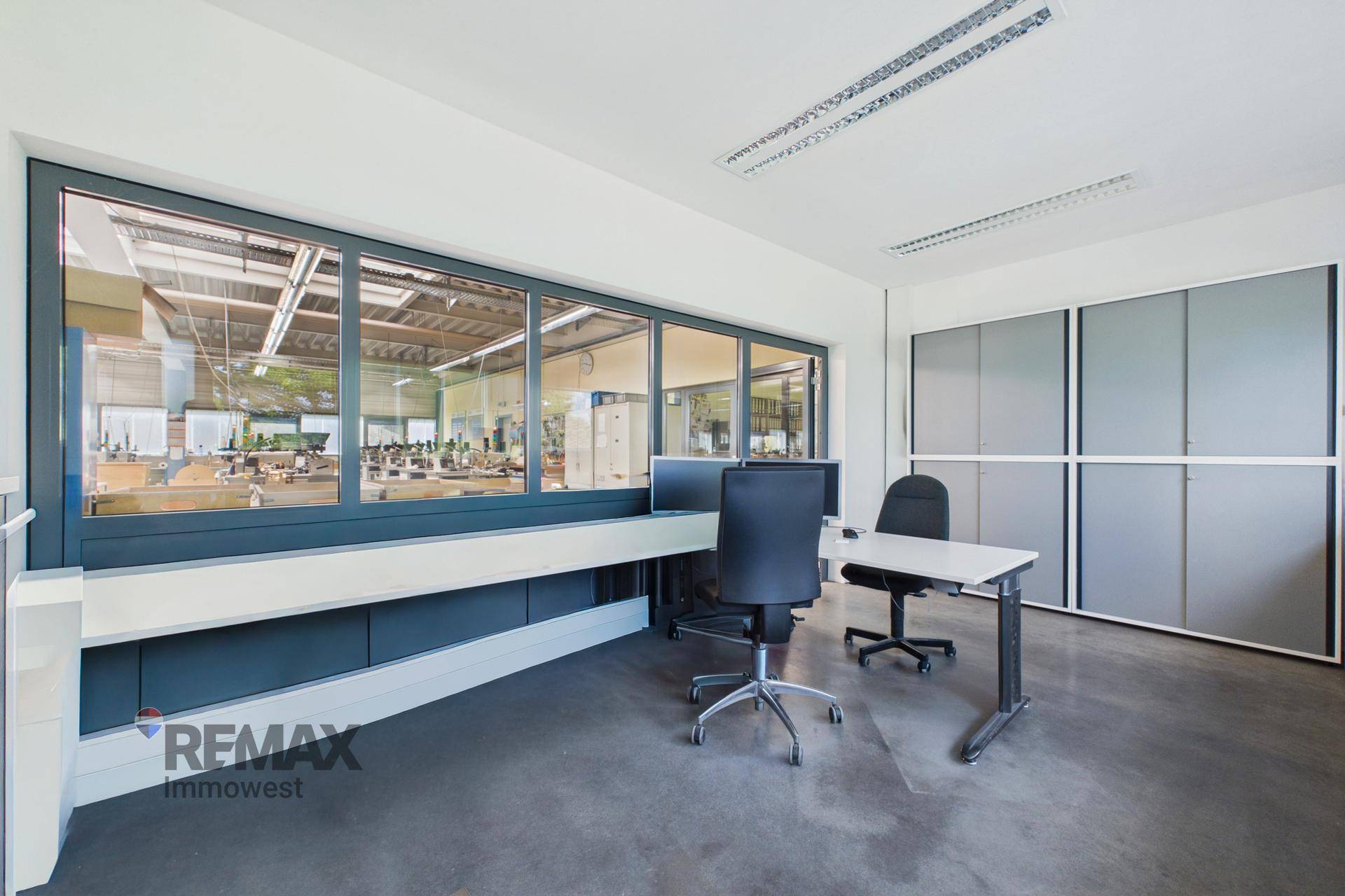 Modernes Büro mit Blick auf die Produktionshalle, ausgestattet mit Schreibtischen und Bürostühlen.