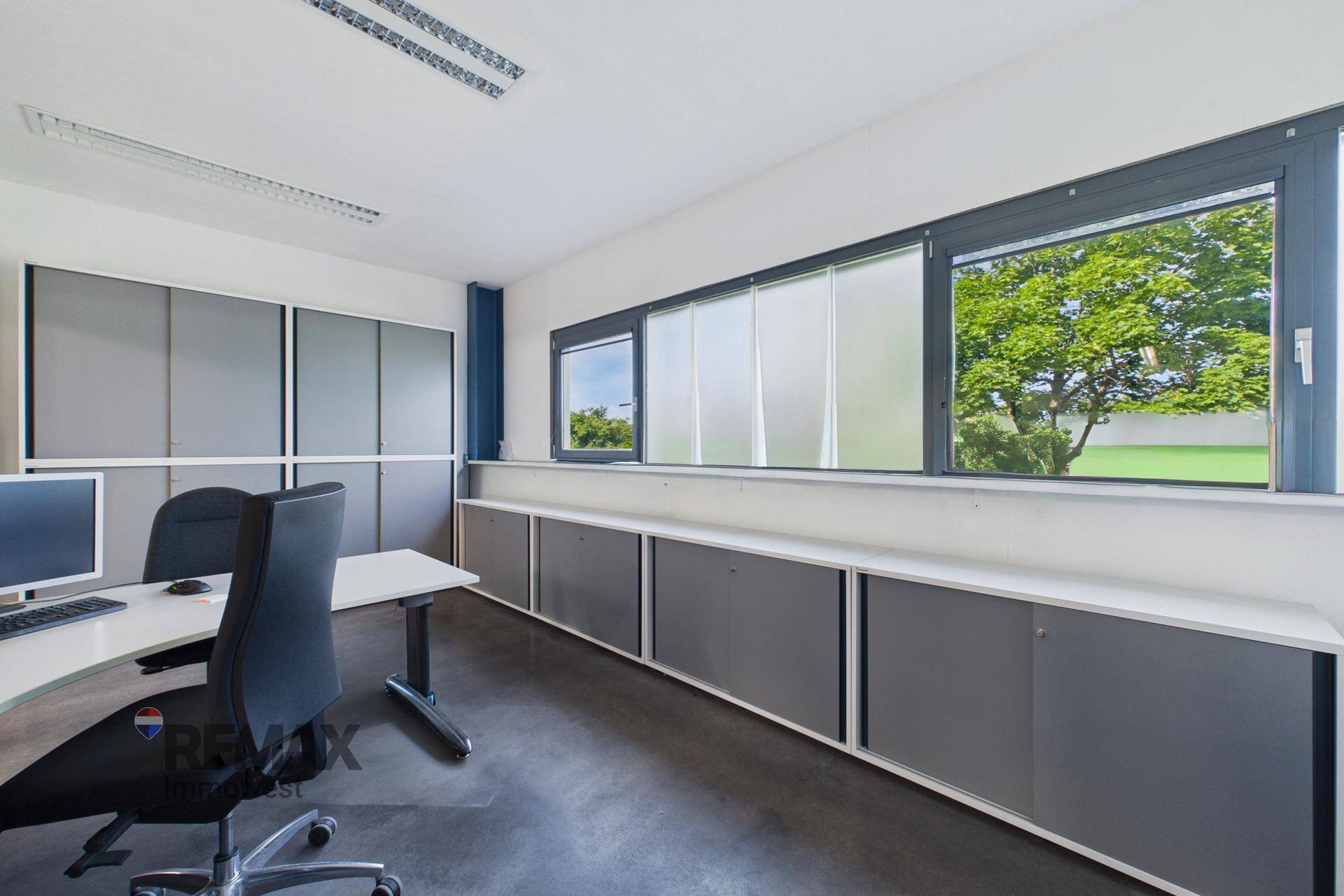 Helles Büro mit großen Fenstern und Blick ins Grüne, ausgestattet mit Schreibtischen und Stauraum.