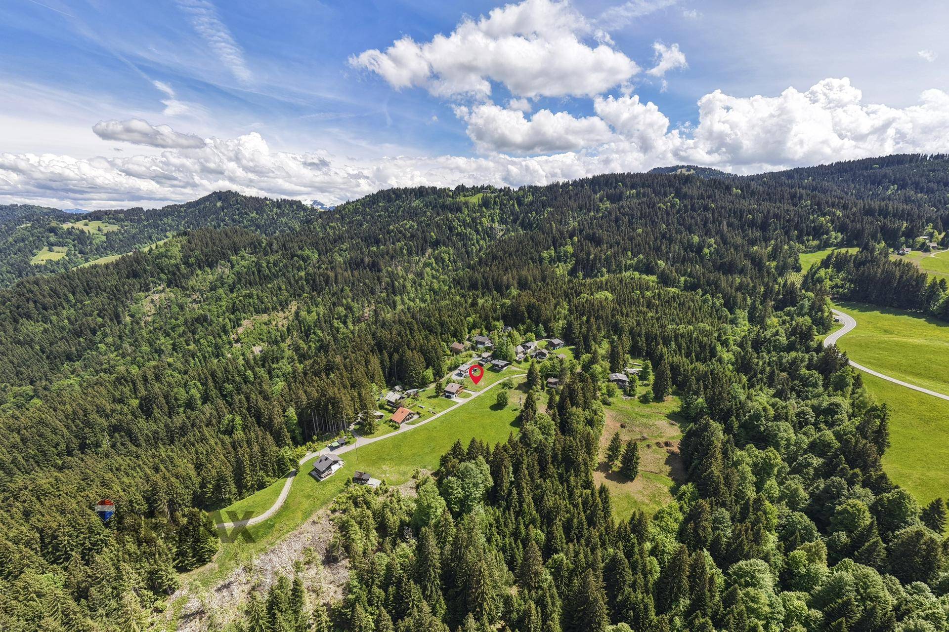 Weitläufige Luftaufnahme einer bewaldeten und hügeligen Landschaft mit einer kleinen Siedlung.