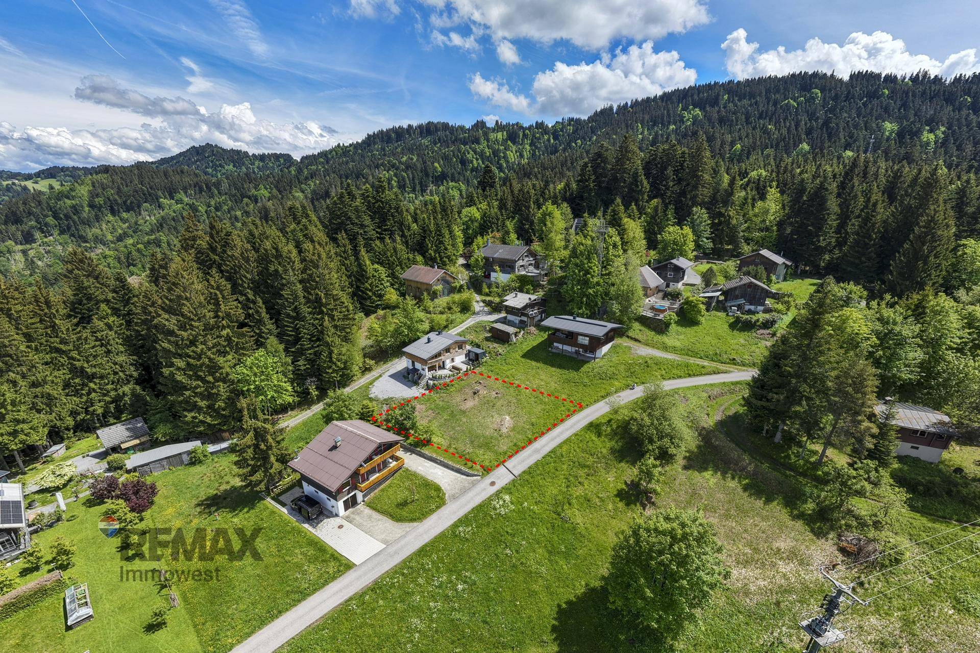 Luftaufnahme eines rot umrandeten Grundstücks, eingebettet zwischen Häusern, Grünflächen und einer Straße.