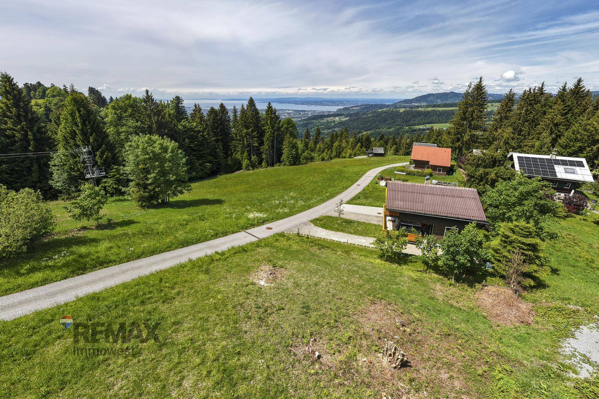 Grüne Hanglage mit einem Weg, Häusern und einem weiten Blick auf den See und die Berge.
