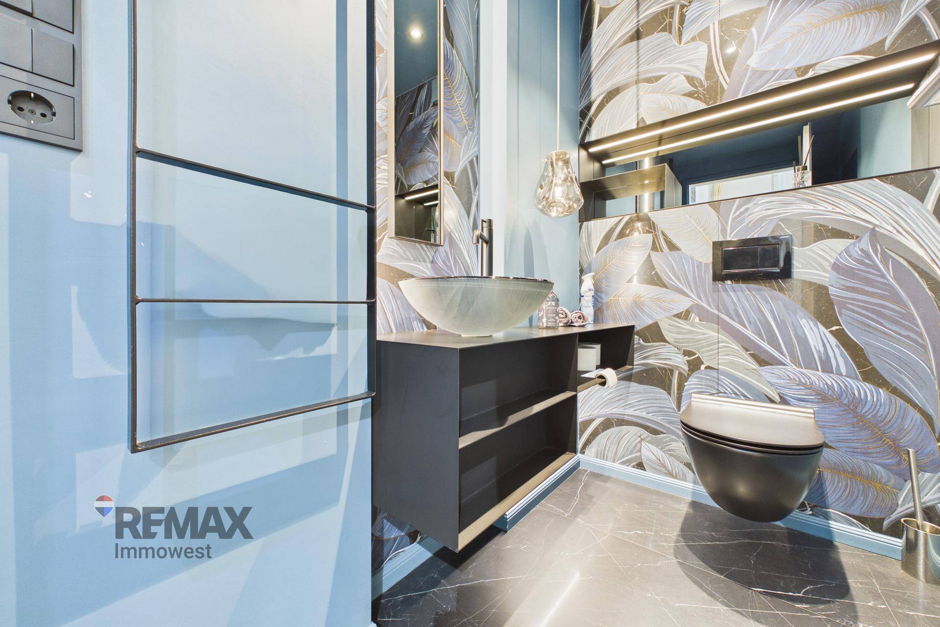 Elegantes Badezimmer mit modernem Waschbecken, wandhängender Toilette und auffälliger Tapete mit Blattmuster.