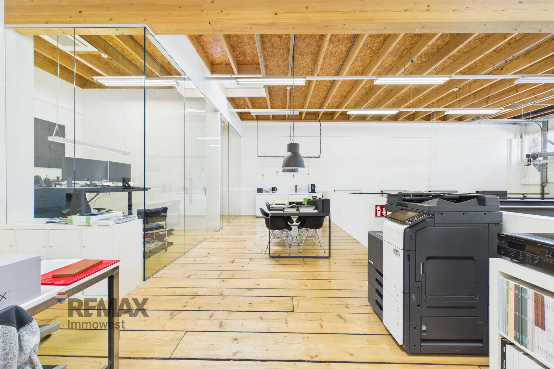 Helles Büro mit Holzbalkendecke, Glaswänden und modernen Arbeitsplätzen.