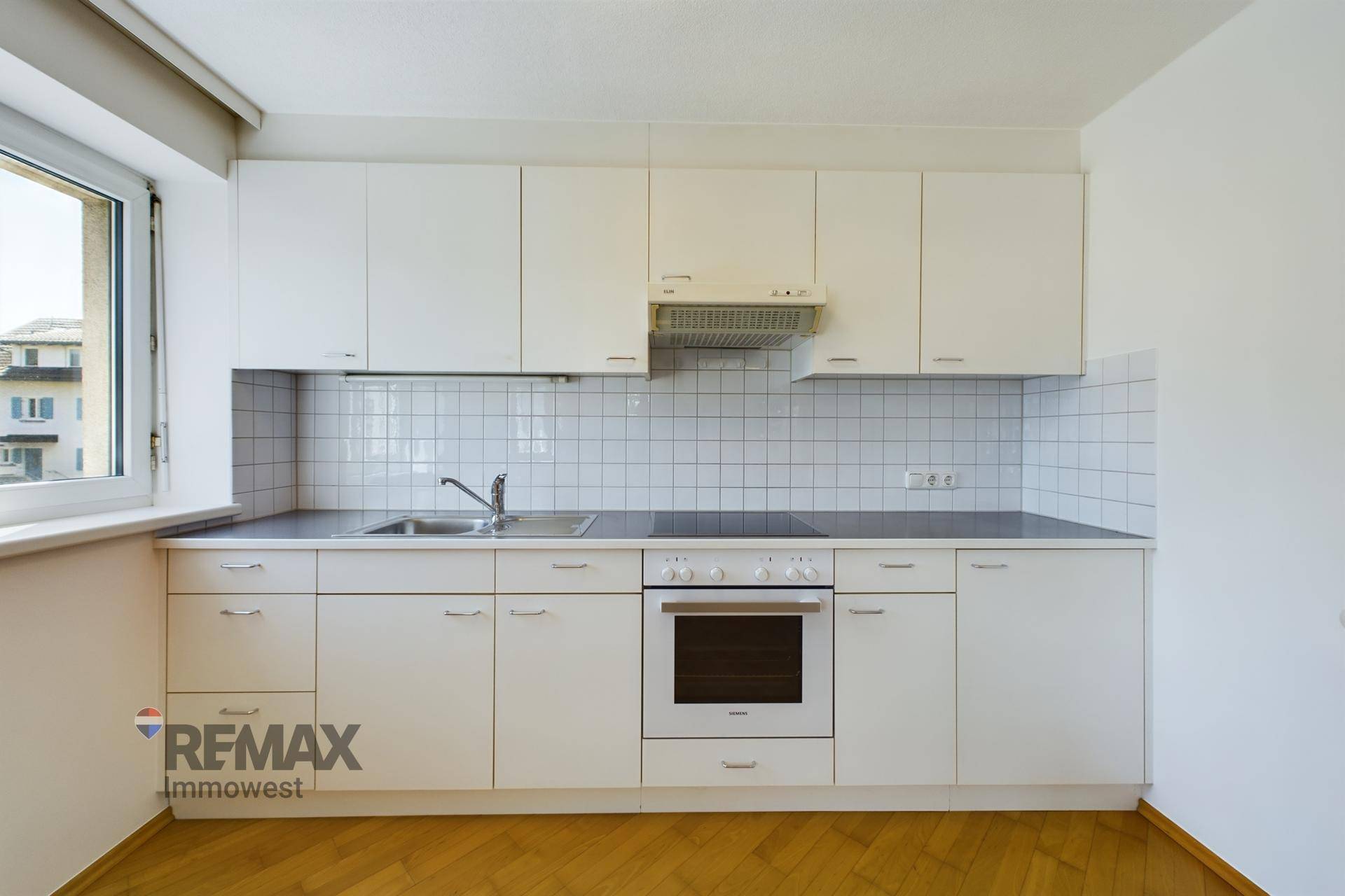 Funktionale Einbauküche mit weißen Schränken, Fliesenrückwand und integrierten Geräten.