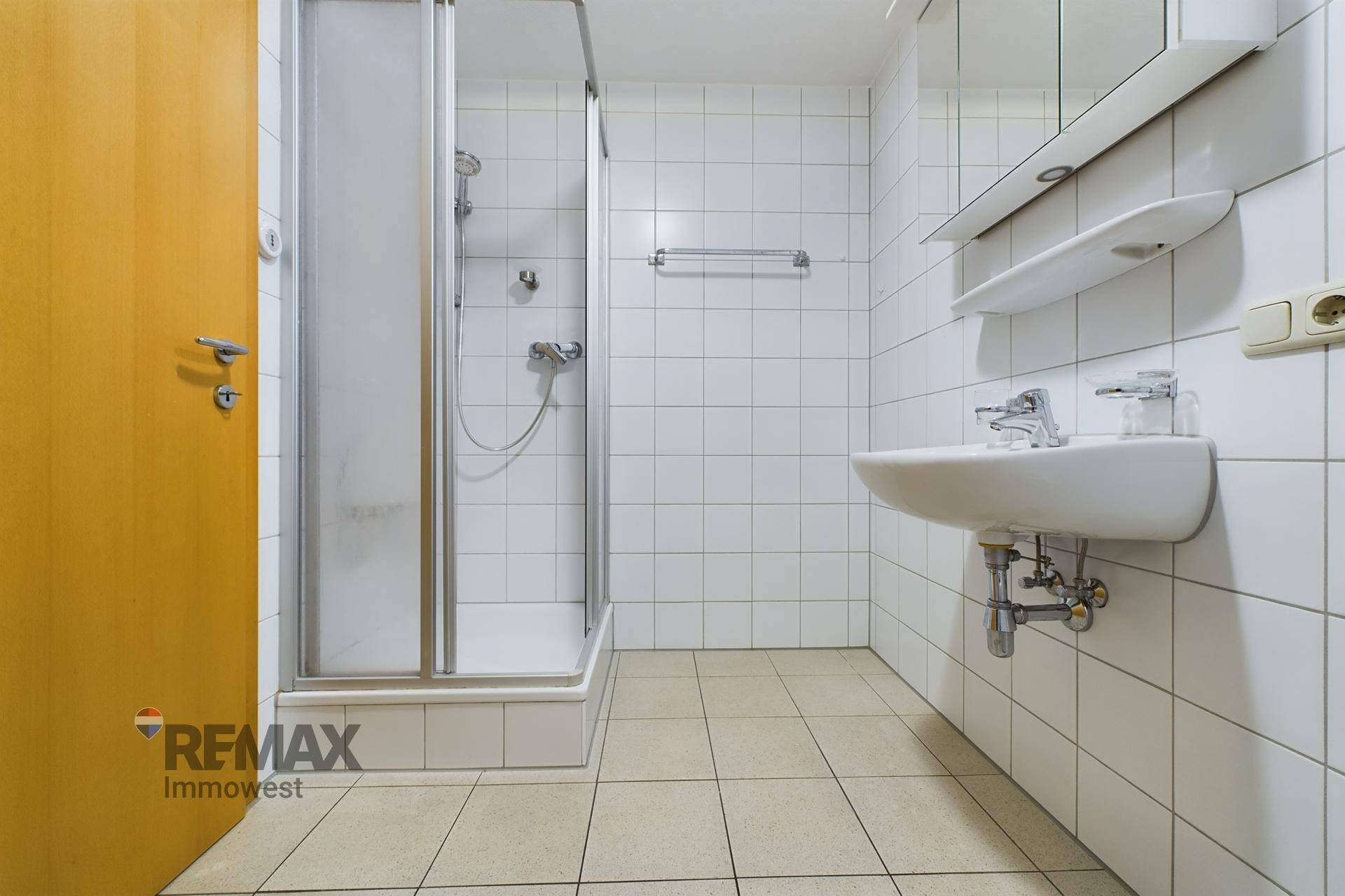 Badezimmer mit Duschkabine, Waschbecken und hellen Wand- und Bodenfliesen.