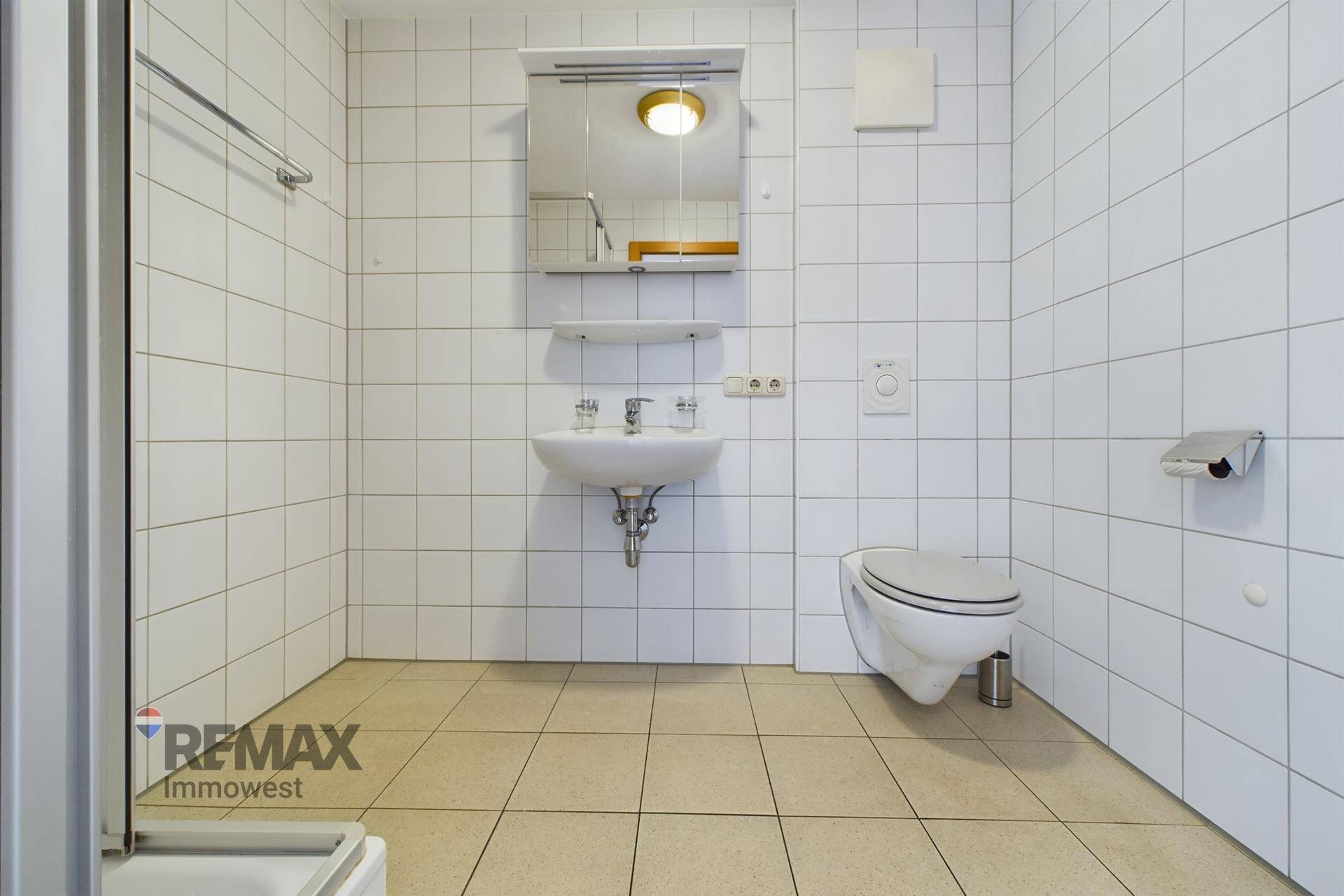 Badezimmer mit WC, Waschbecken und Spiegelschrank, komplett gefliest in hellen Farben.