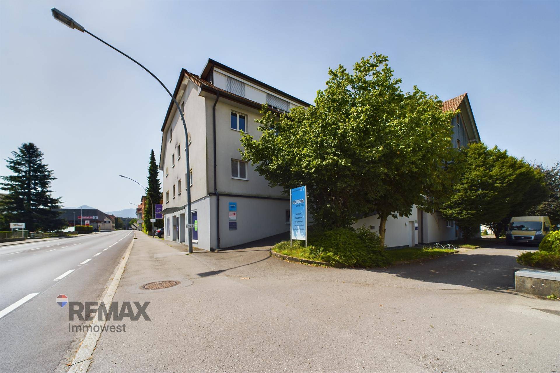 Gebäudeansicht von der Straße aus mit Bäumen und einem Schild.