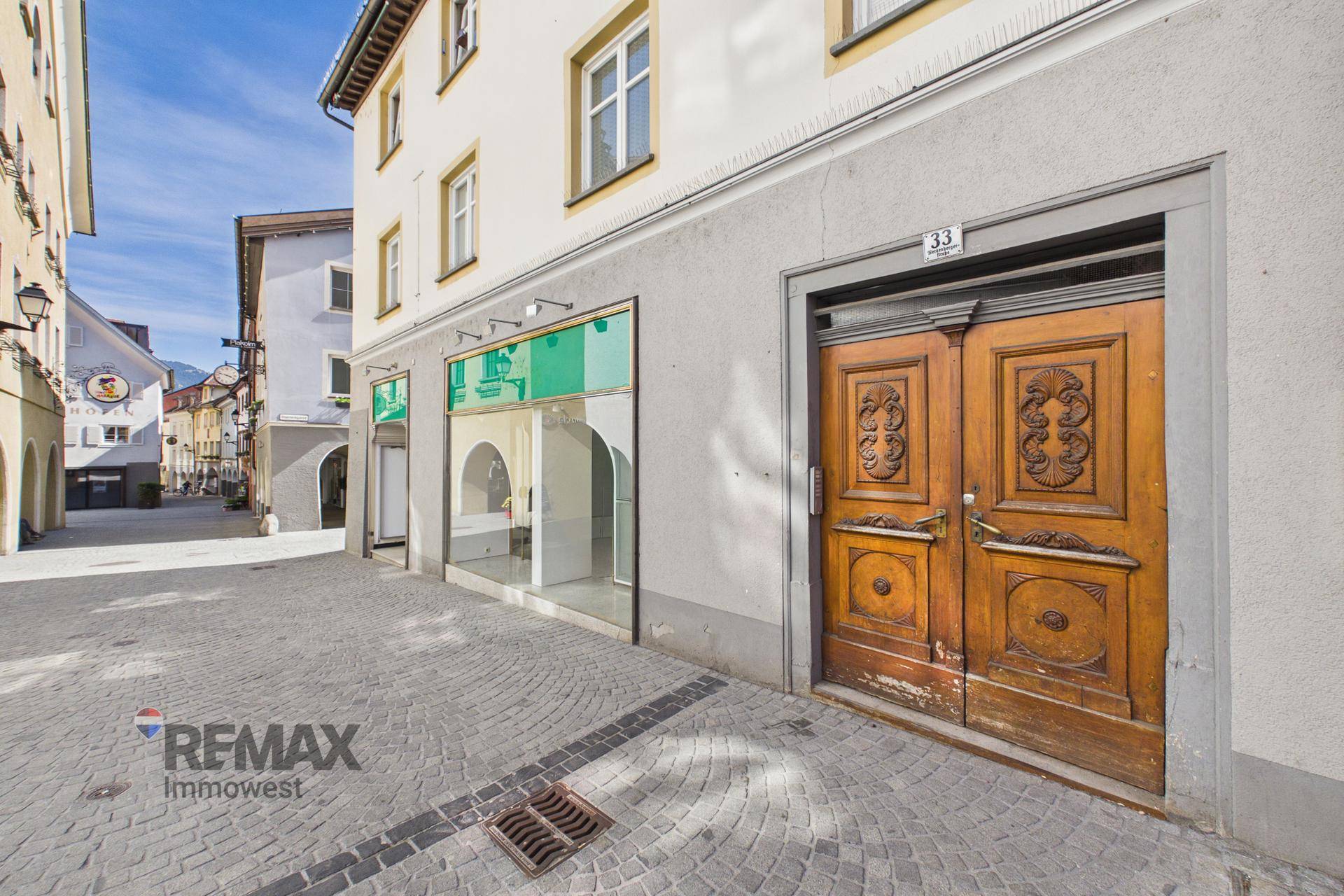 Historische Fassade mit einer kunstvoll geschnitzten Holztür und großen Schaufenstern daneben.