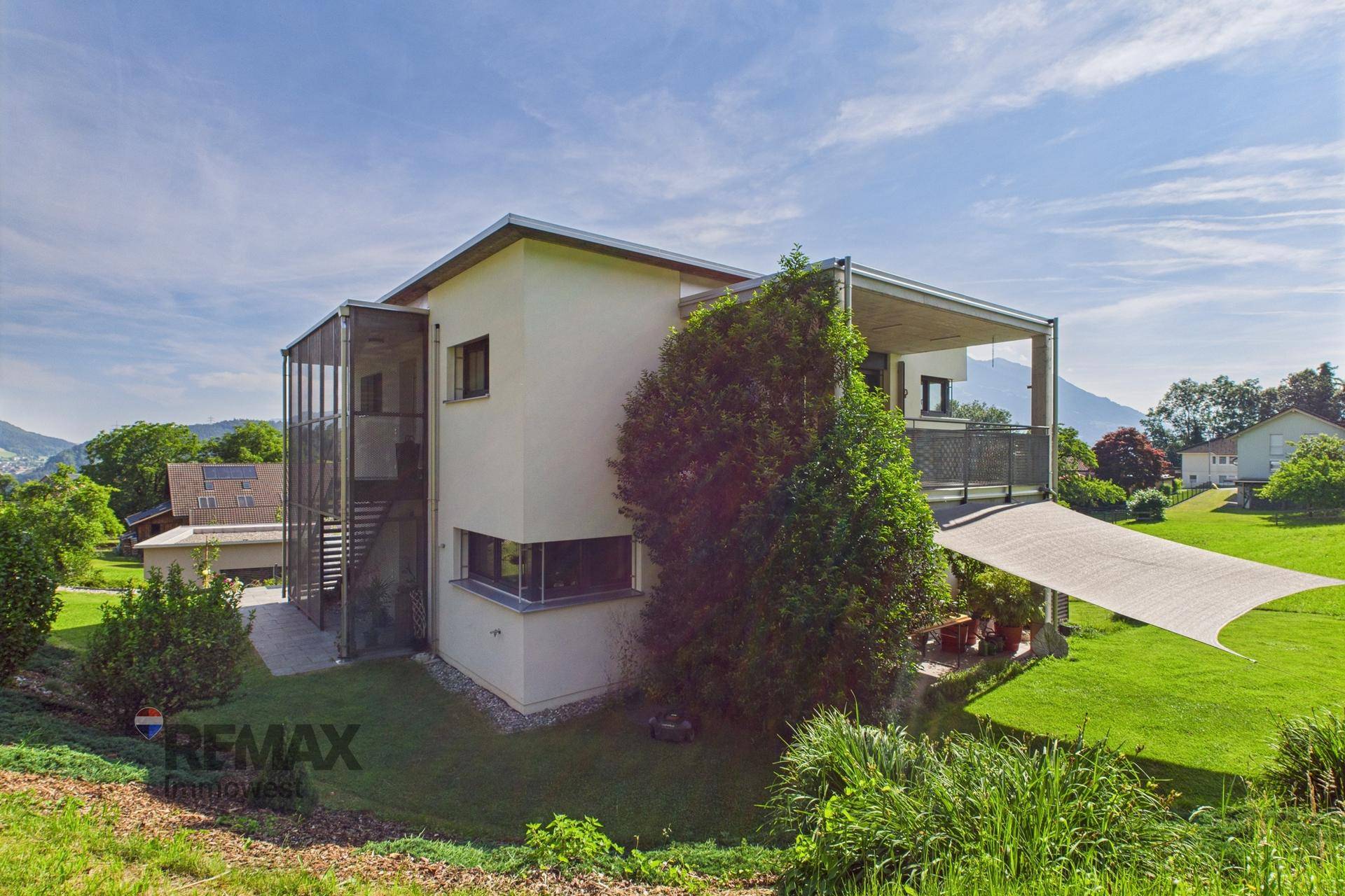 Modernes Wohnhaus mit mehreren Balkonen und einer überdachten Terrasse im Grünen.