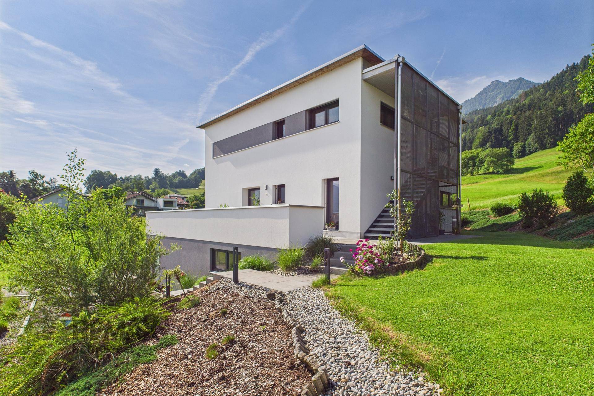 Seitliche Ansicht des modernen Hauses mit Zugang zum Garten und Bergblick.