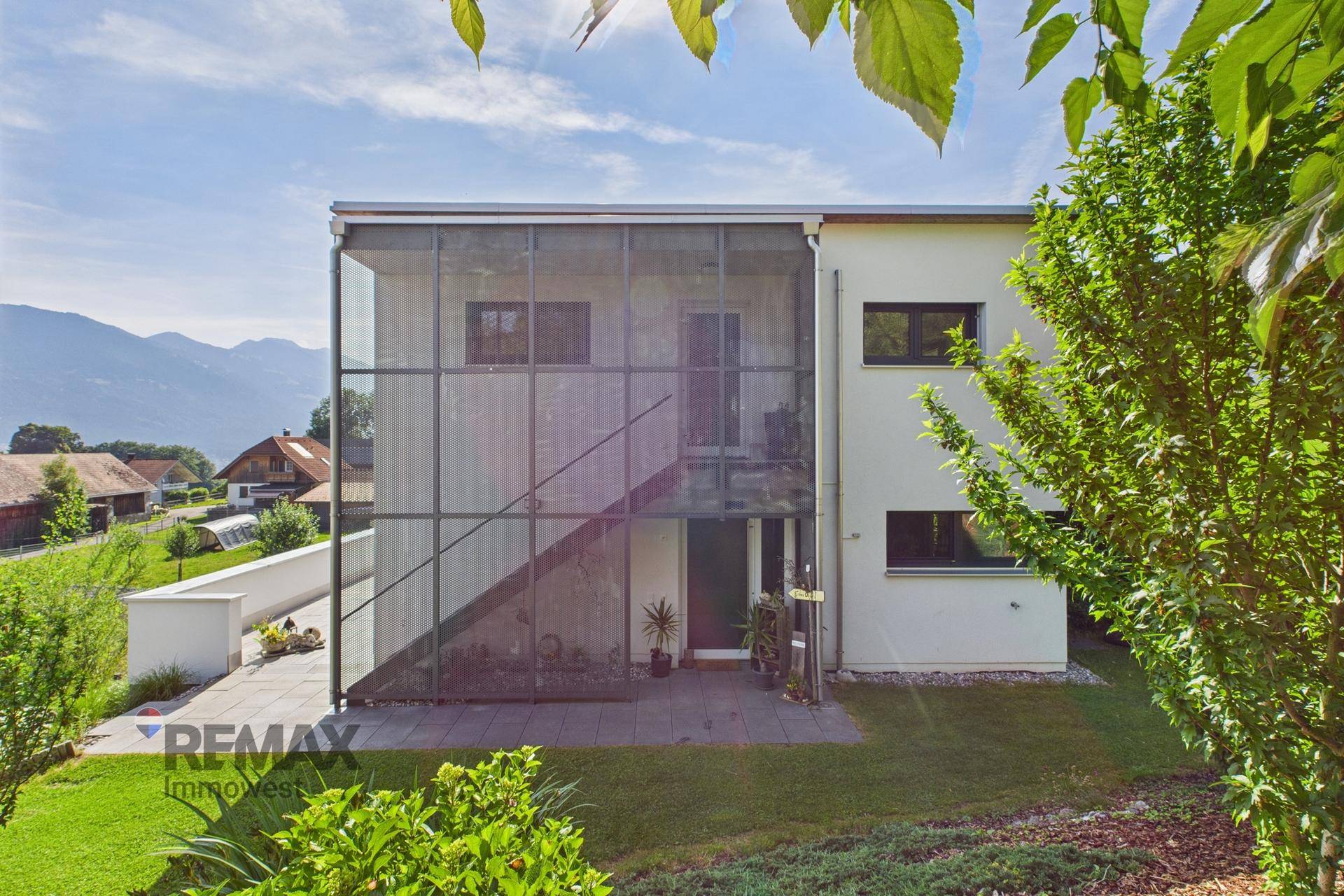 Rückansicht des modernen Hauses mit großer Glasfassade und Zugang zum Garten.