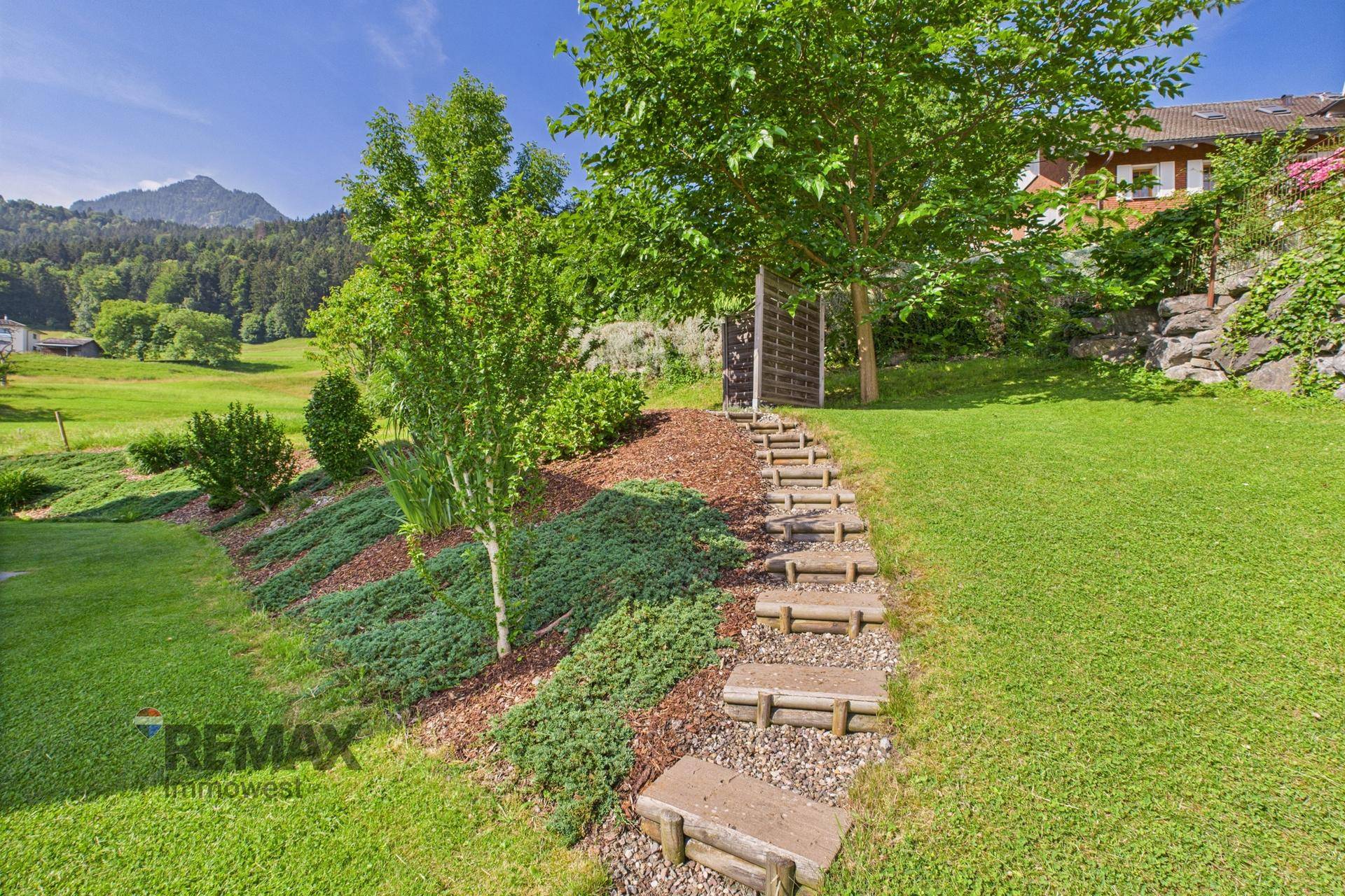 Naturnaher Garten mit Holzstufen, Bäumen und Sträuchern, eingebettet in die Landschaft.