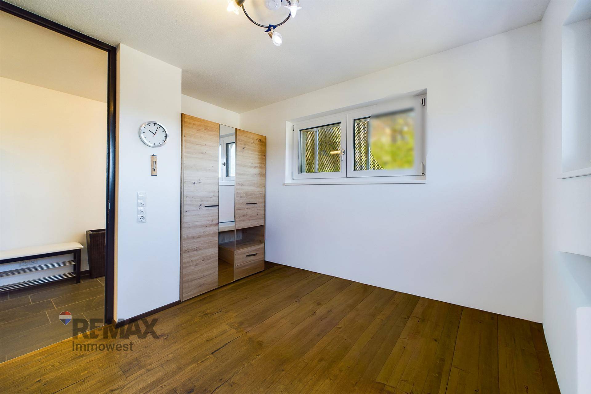 Helles Schlafzimmer mit Holzboden, Einbauschrank und Fenster mit Blick ins Grüne.