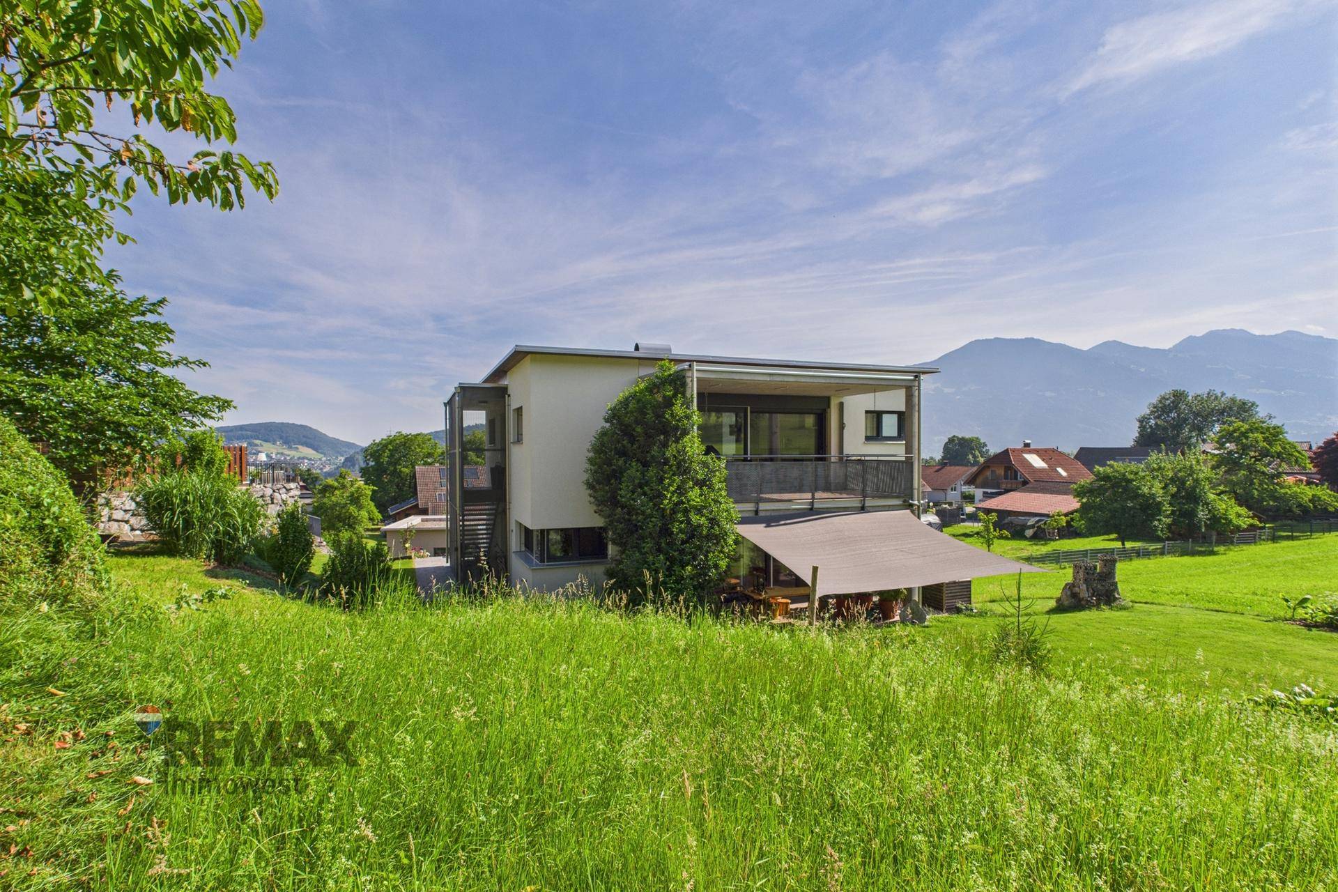 Modernes Wohnhaus mit Balkonen und überdachter Terrasse in idyllischer Hügellandschaft.
